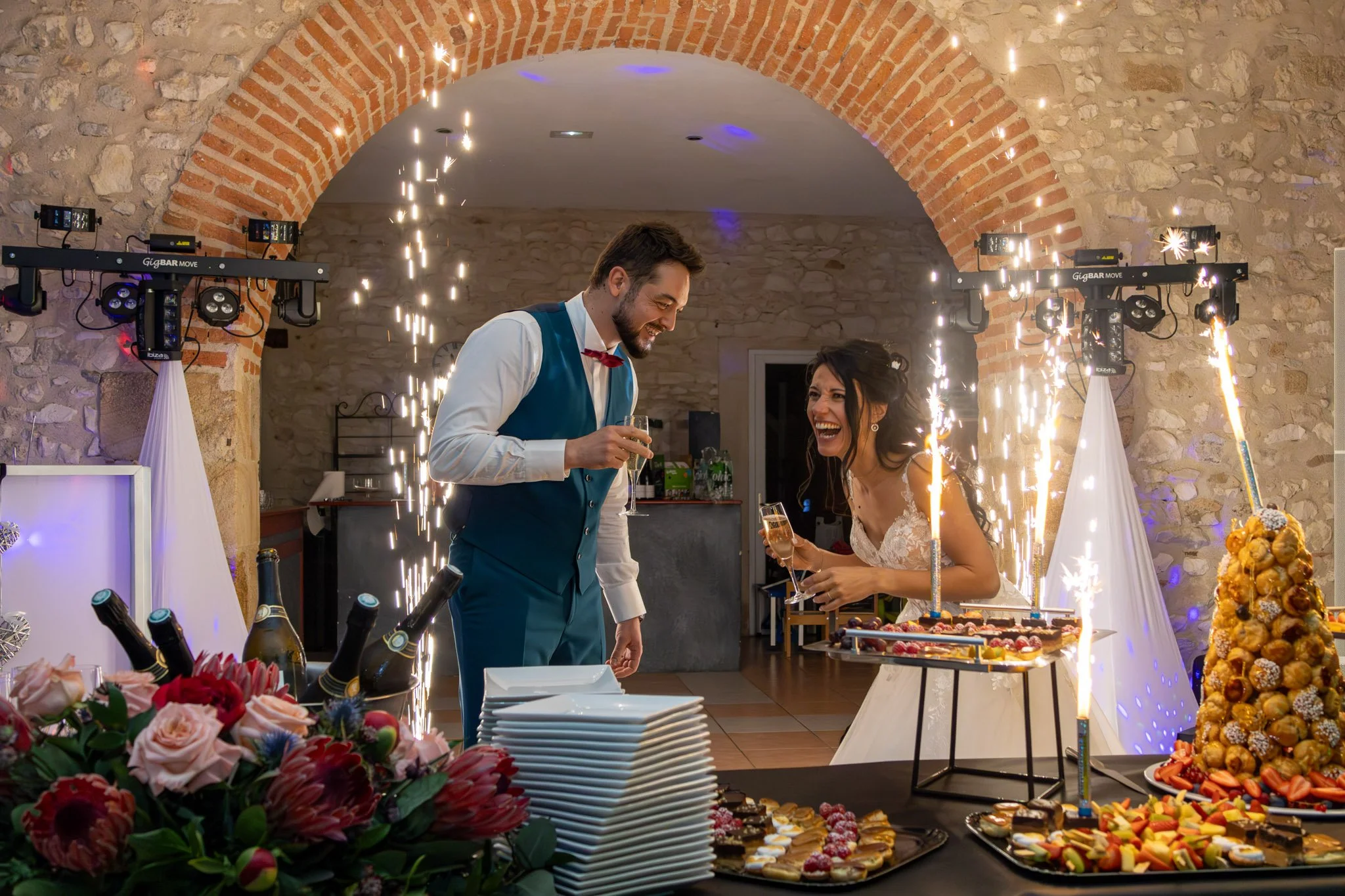 Mariés qui rigolent coupes de champagne à la main et bougies fontaines à gateau