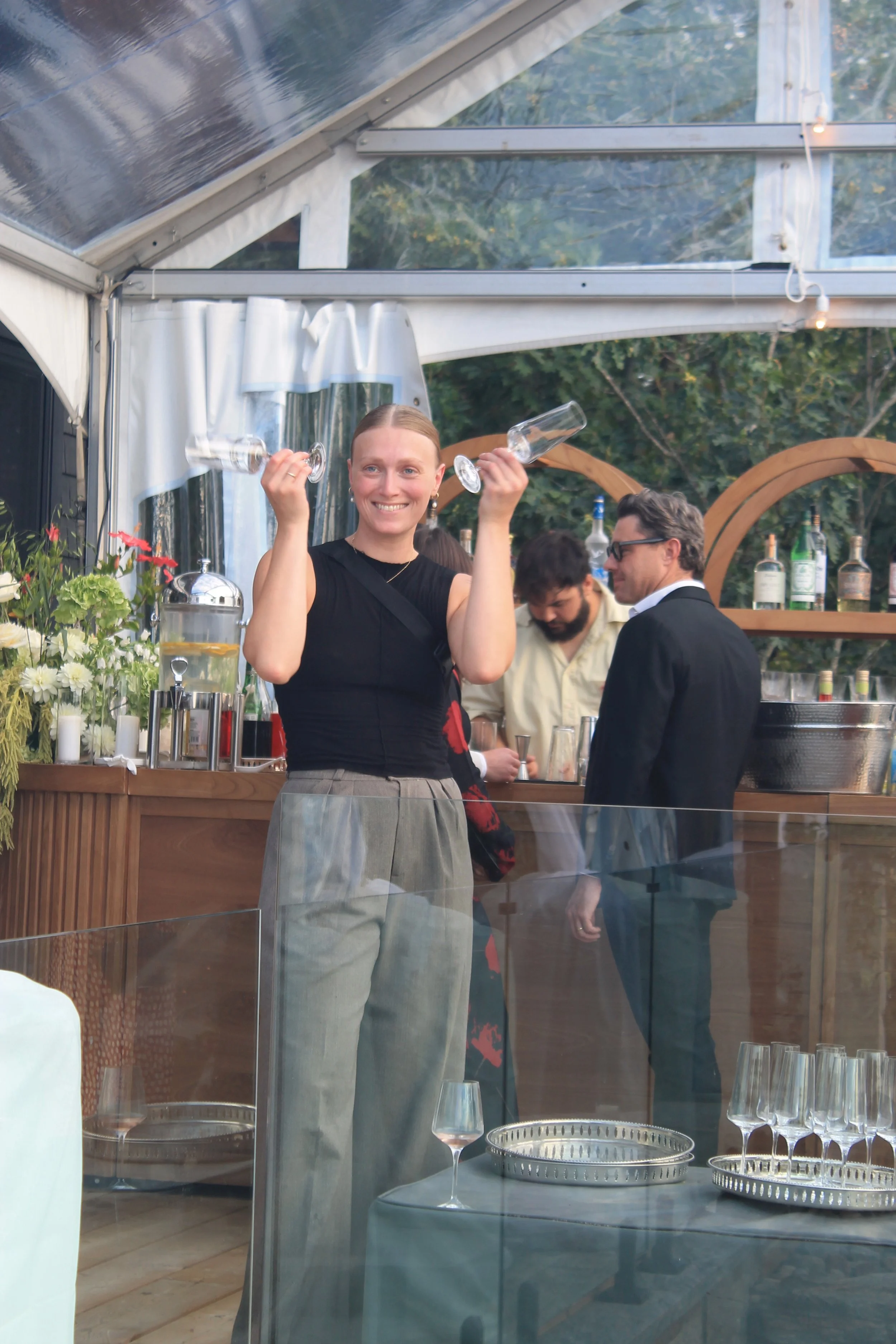 Emma, Service Manager and owner, holds two champagne flutes up to her head in a playfulway
