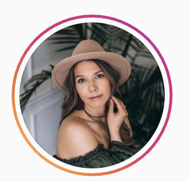 A woman wearing a tan hat and an off-the-shoulder top, with a plant in the background.