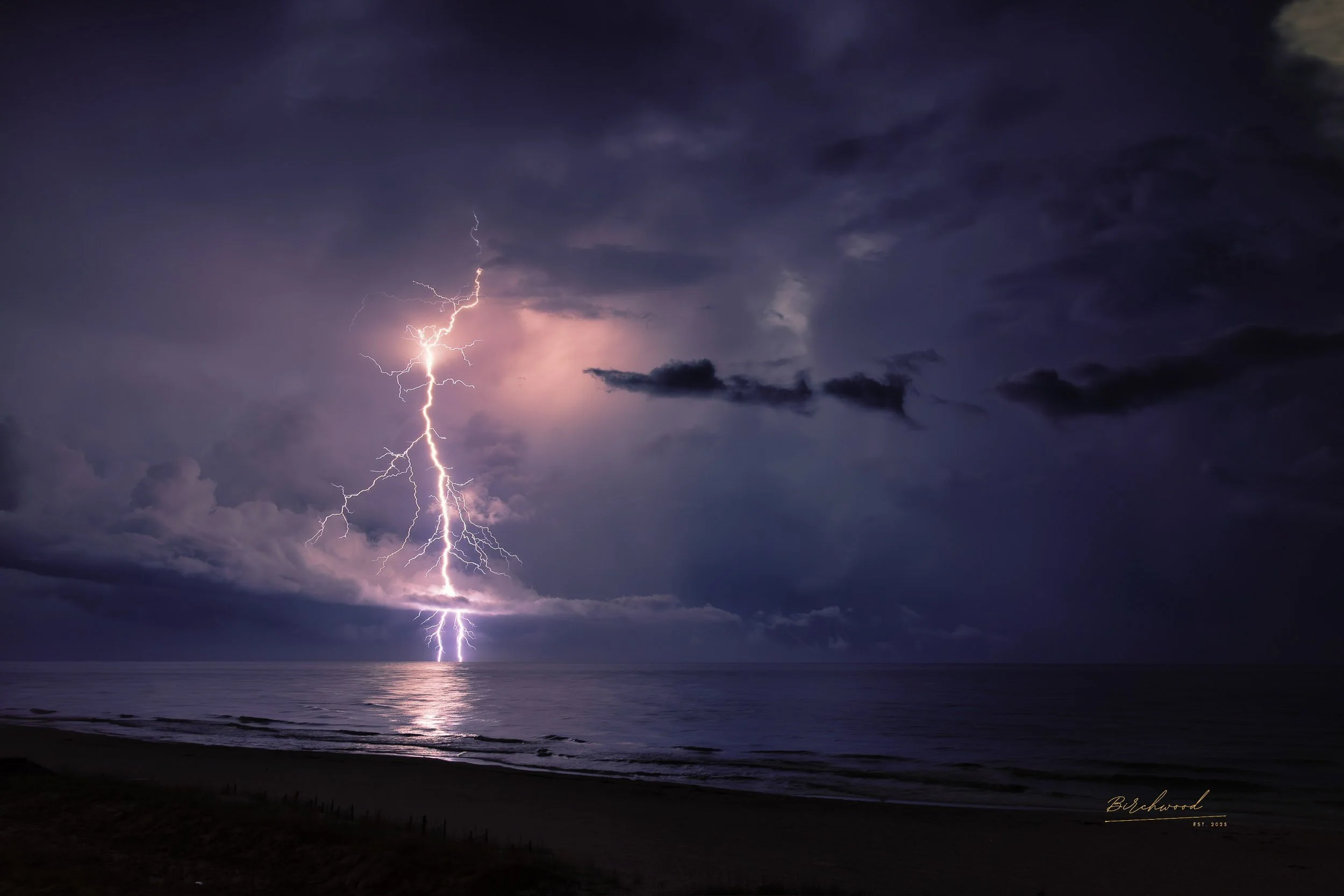 Lightning storm over the gulf of America at night with dark clouds and a reflection on the water.