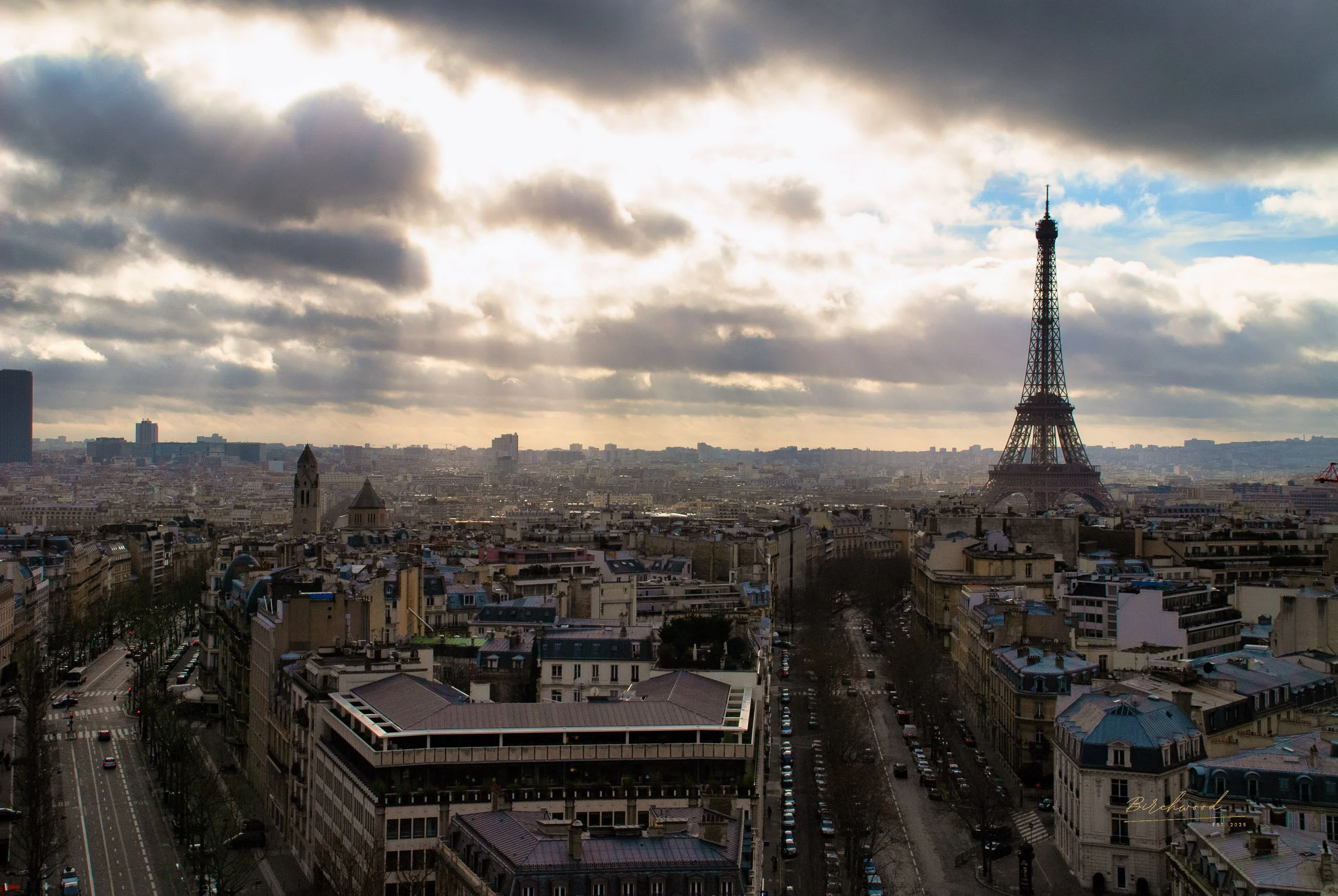 A wide view of Paris, France, with the Eiffel Tower in the distance under a partly cloudy sky during daytime.