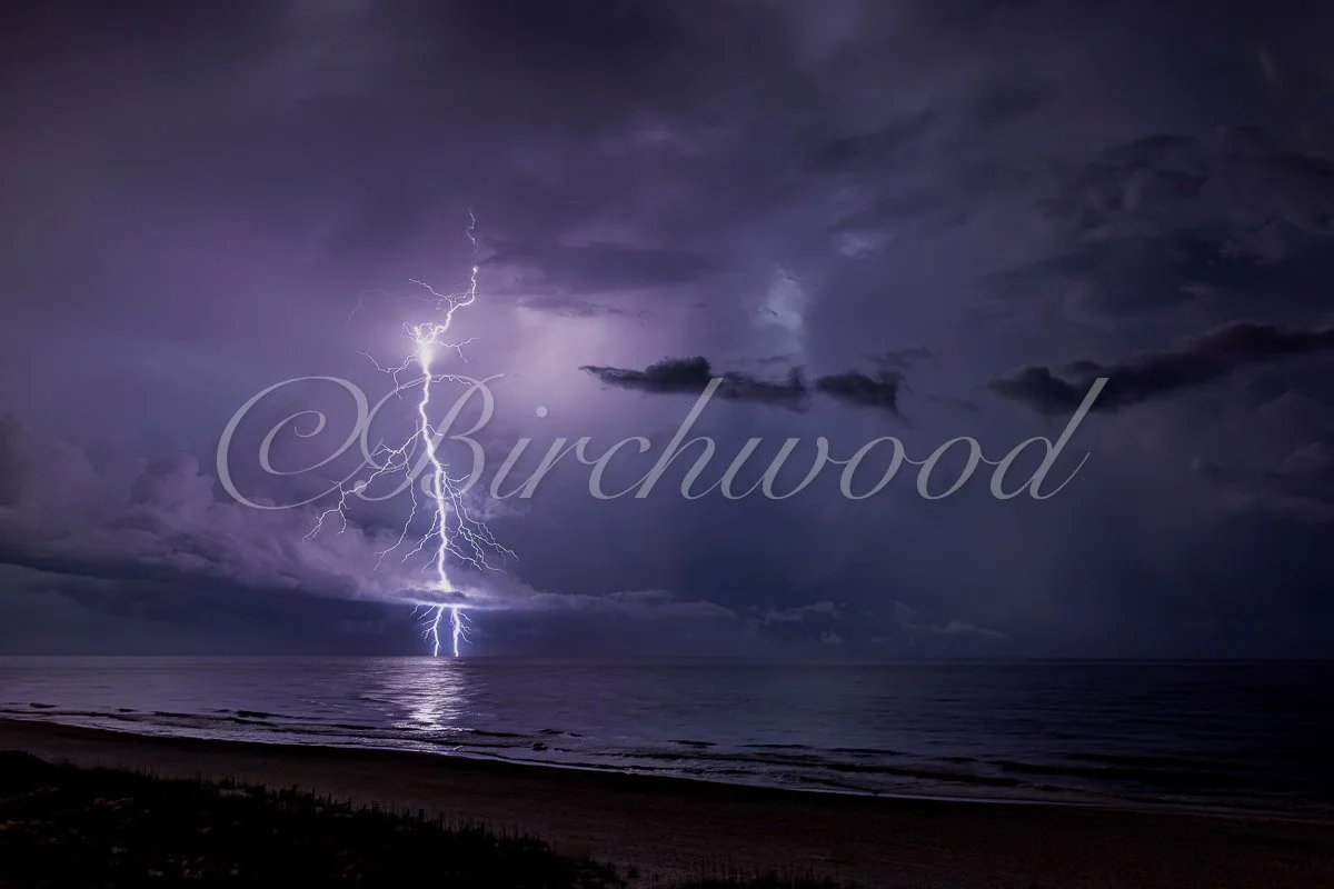 Lightning strikes over the ocean at night with dark clouds in the sky.
