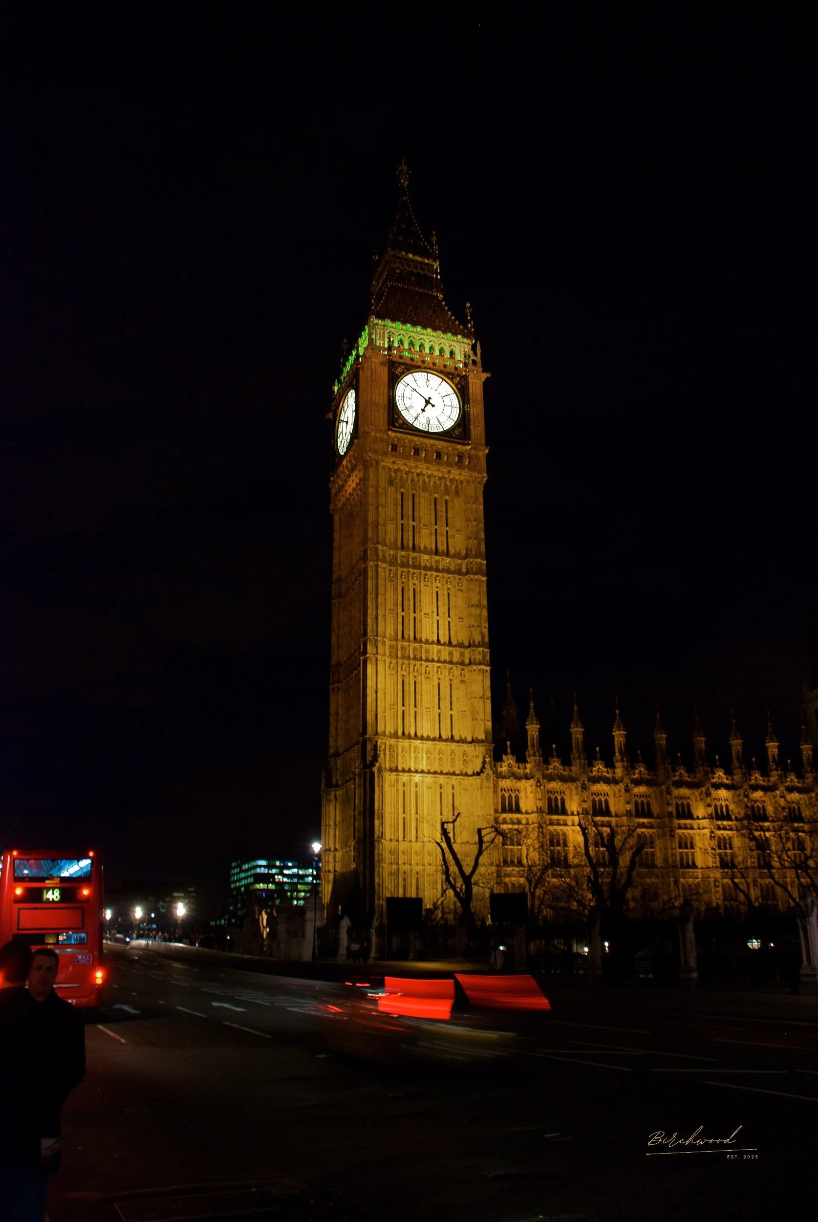Nighttime photo of Big Ben clock tower in London, illuminated with green and yellow lights, with a dark sky in the background.