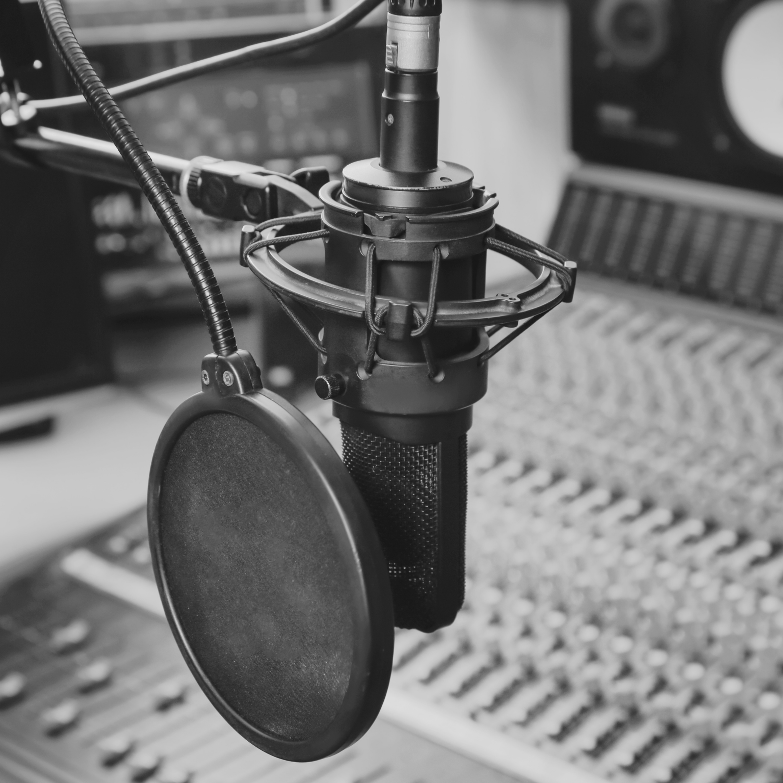 Foreground: In focus radio station microphone with a pop filter. Background: out of focus sound control board.