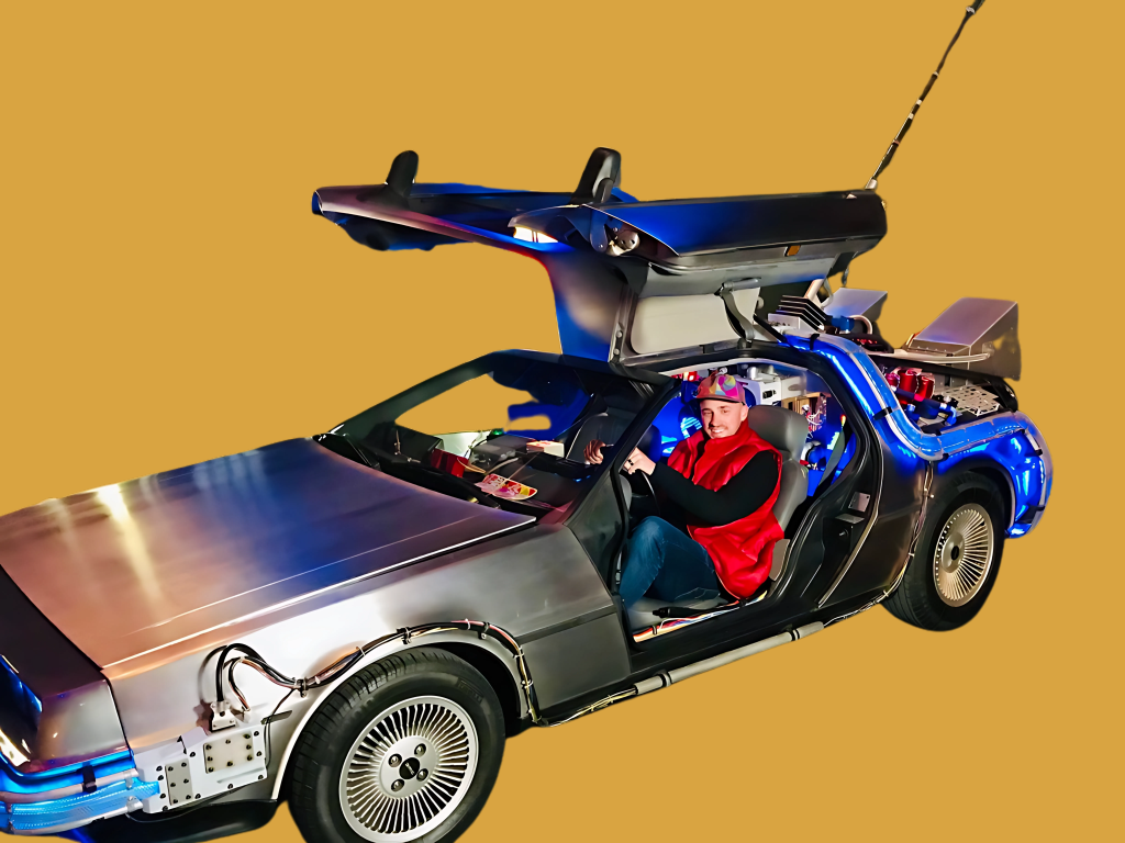 DeLorean time machine from the movie Back to the Future with Jesse Freitas dressed as the character Marty McFly sitting in the driver's seat, against a solid yellow background.
