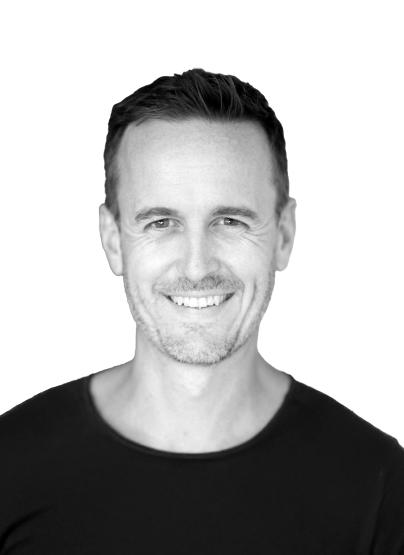 Black and white portrait of a smiling man with short hair, wearing a black shirt, against a plain white background.