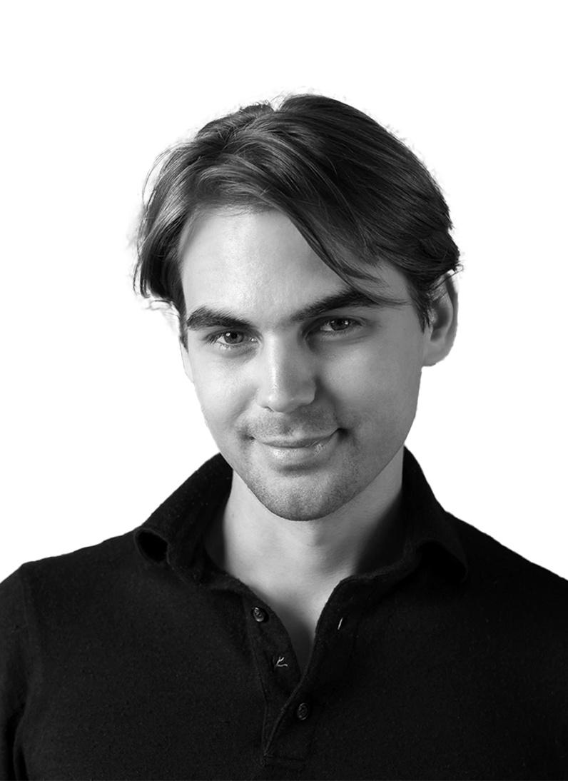 Black and white portrait of a young man with dark hair, wearing a black collared shirt, smiling slightly against a plain white background.