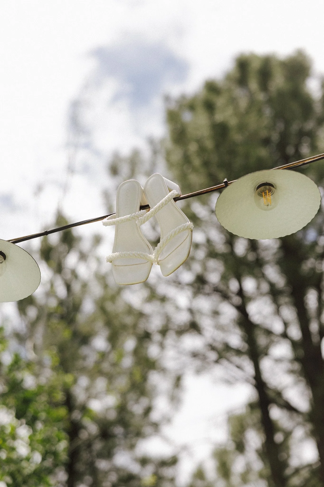 A clothesline with white gloves and paper lanterns hanging outdoors, with blurred trees and sky in the background.