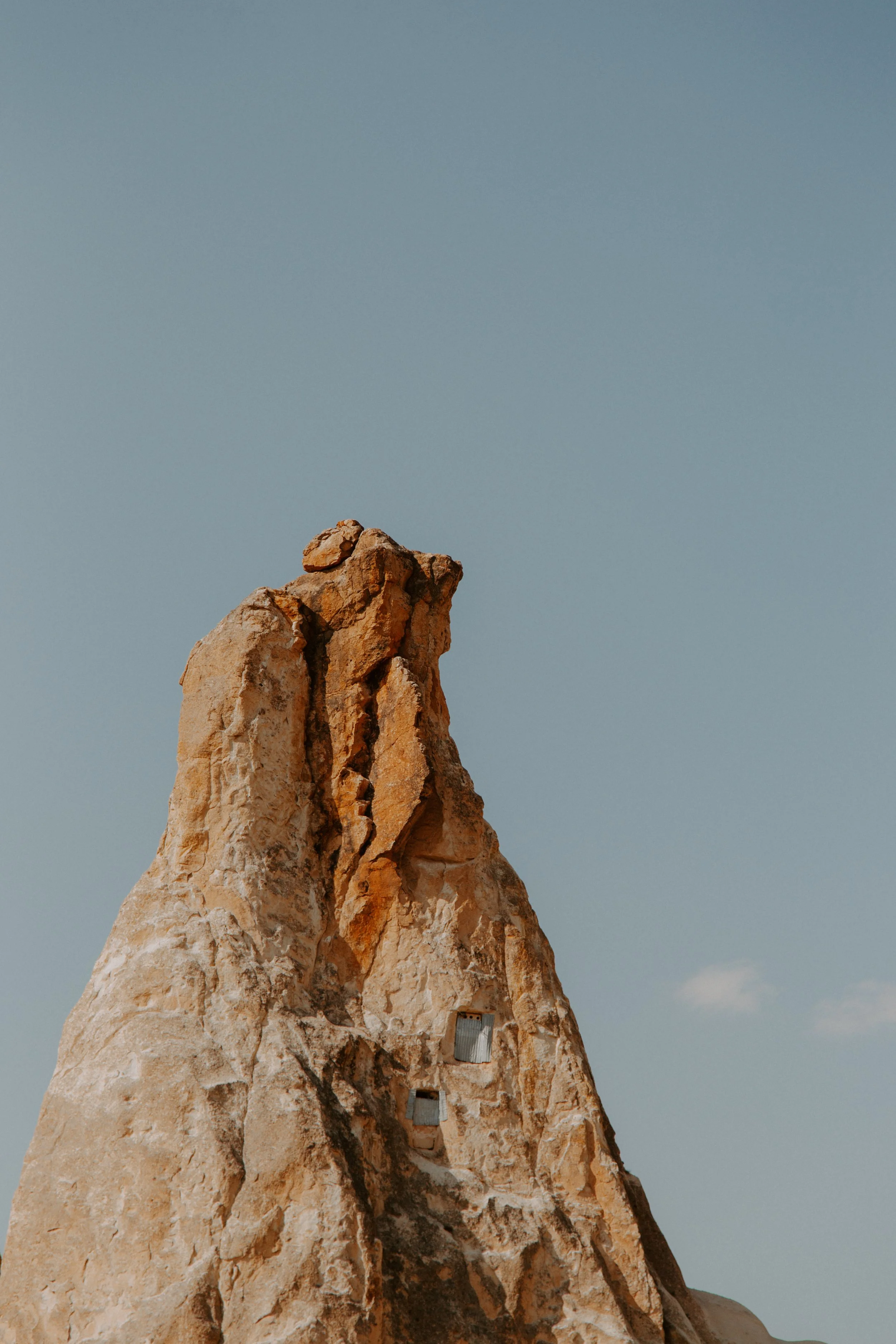 Close-up of a rocky mountain with two small, metallic-looking structures built into the cliff face, against a pale blue sky.