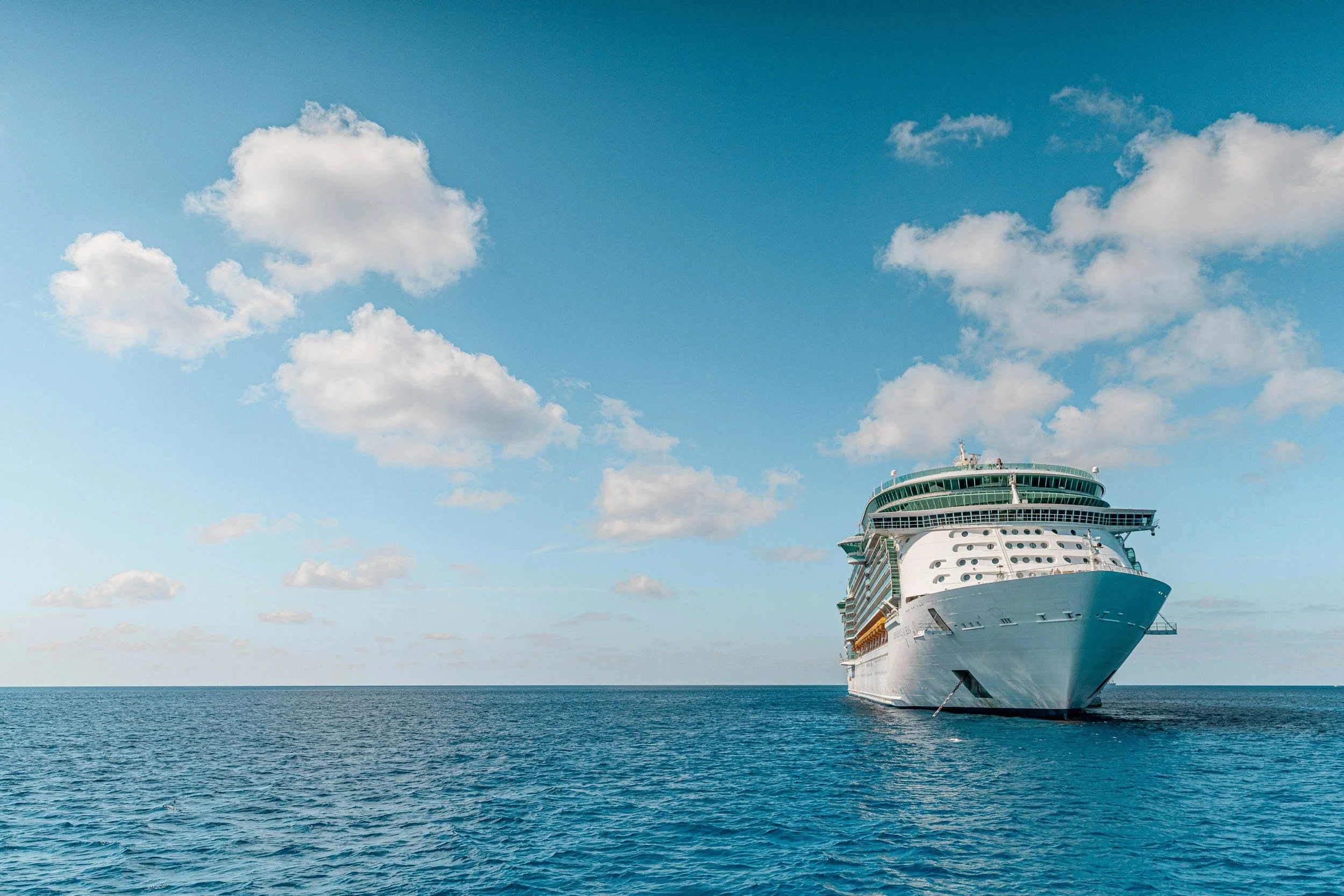 Large white cruise ship sailing on the ocean with a blue sky and scattered clouds above.