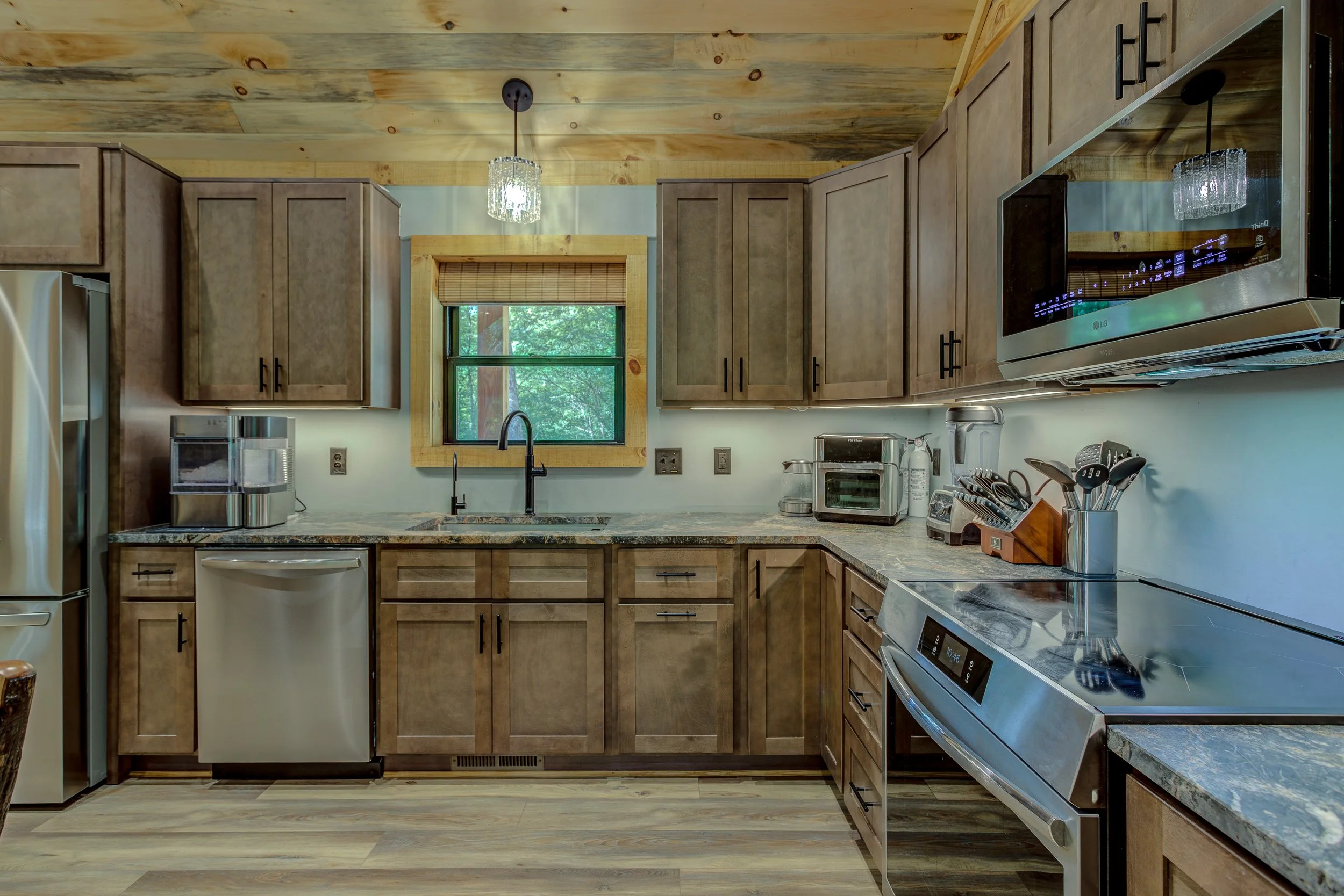 A spacious country kitchen designed for gathering, featuring custom wood cabinetry, stainless-steel appliances, generous counter space, and a large island with plenty of seating. The beautiful wood ceiling and open layout bring warmth and rustic char