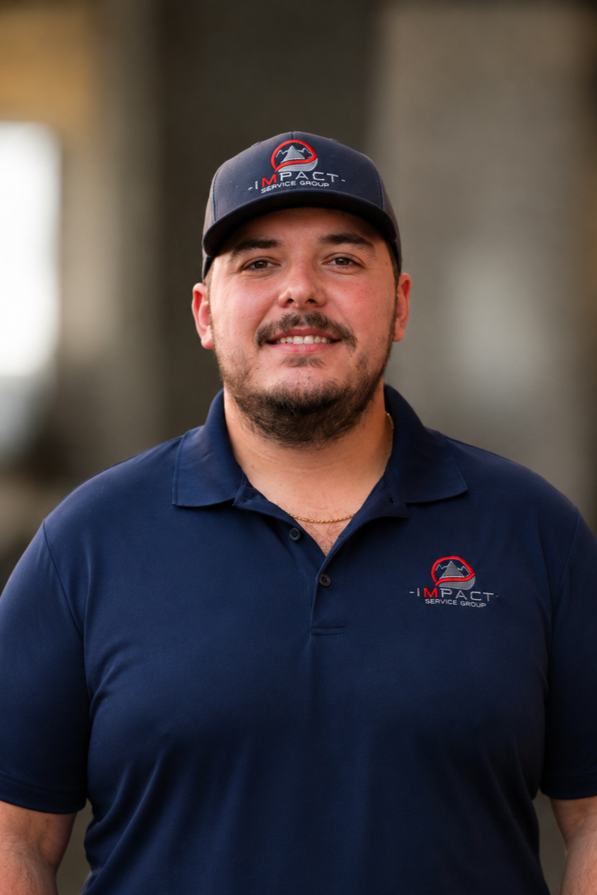 A man wearing a navy blue polo shirt and a baseball cap with a logo, standing outside near brick walls and a window.