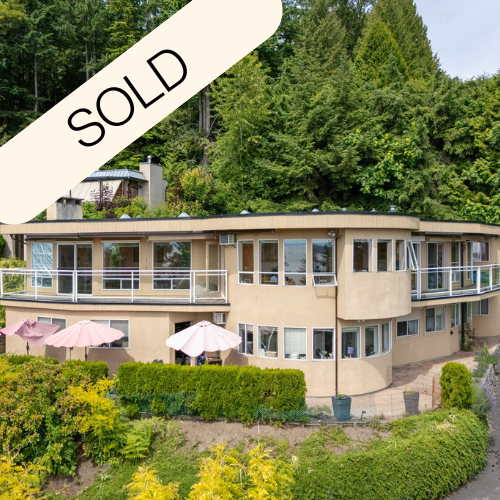 A residential house with two balconies, surrounded by trees and greenery, with patio umbrellas in the front yard, and a 'Sold' banner across the top left corner.