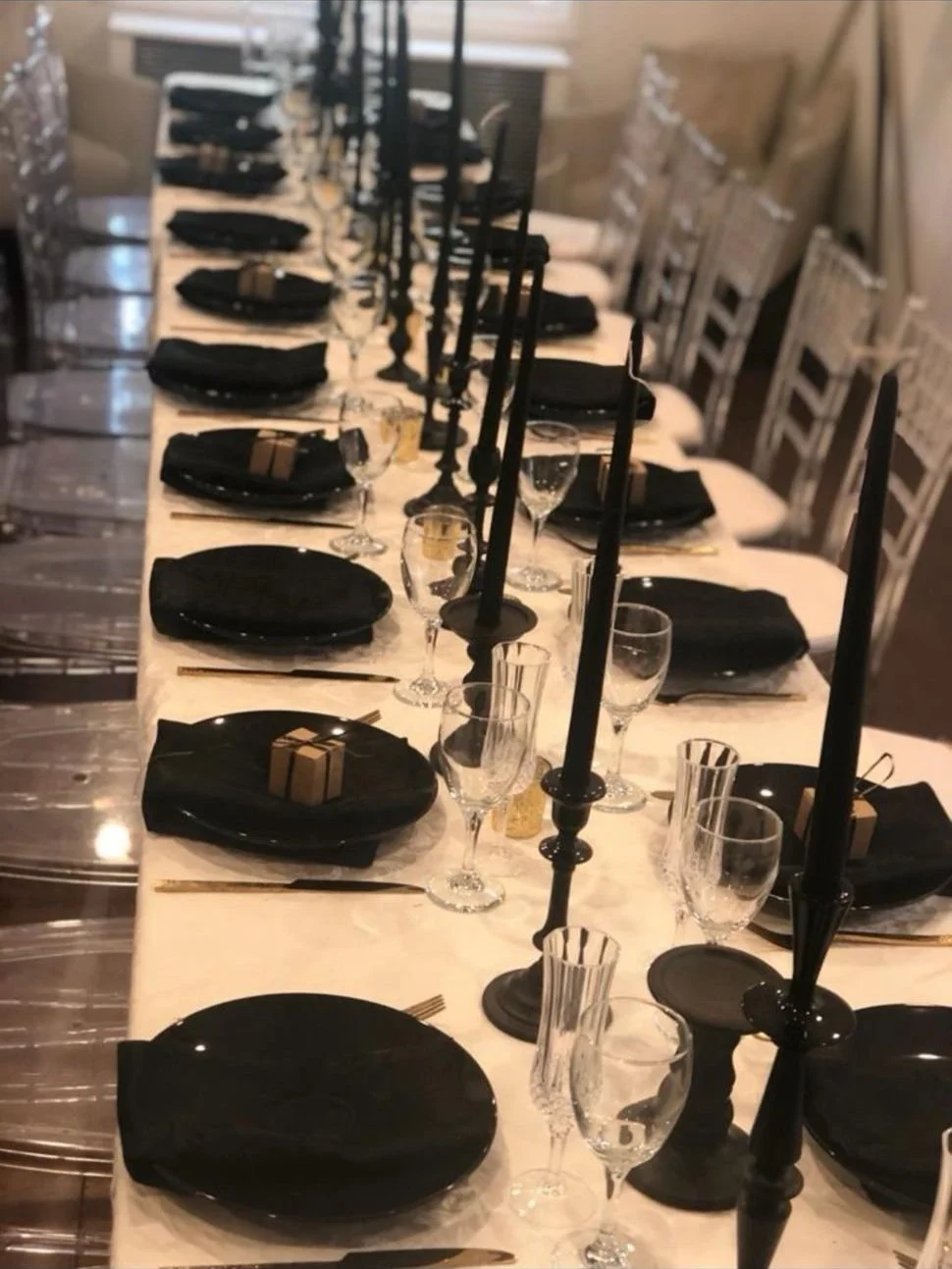 A long dining table set for a formal dinner with black plates, black napkins, multiple glasses, and tall black candlesticks with unlit black candles.