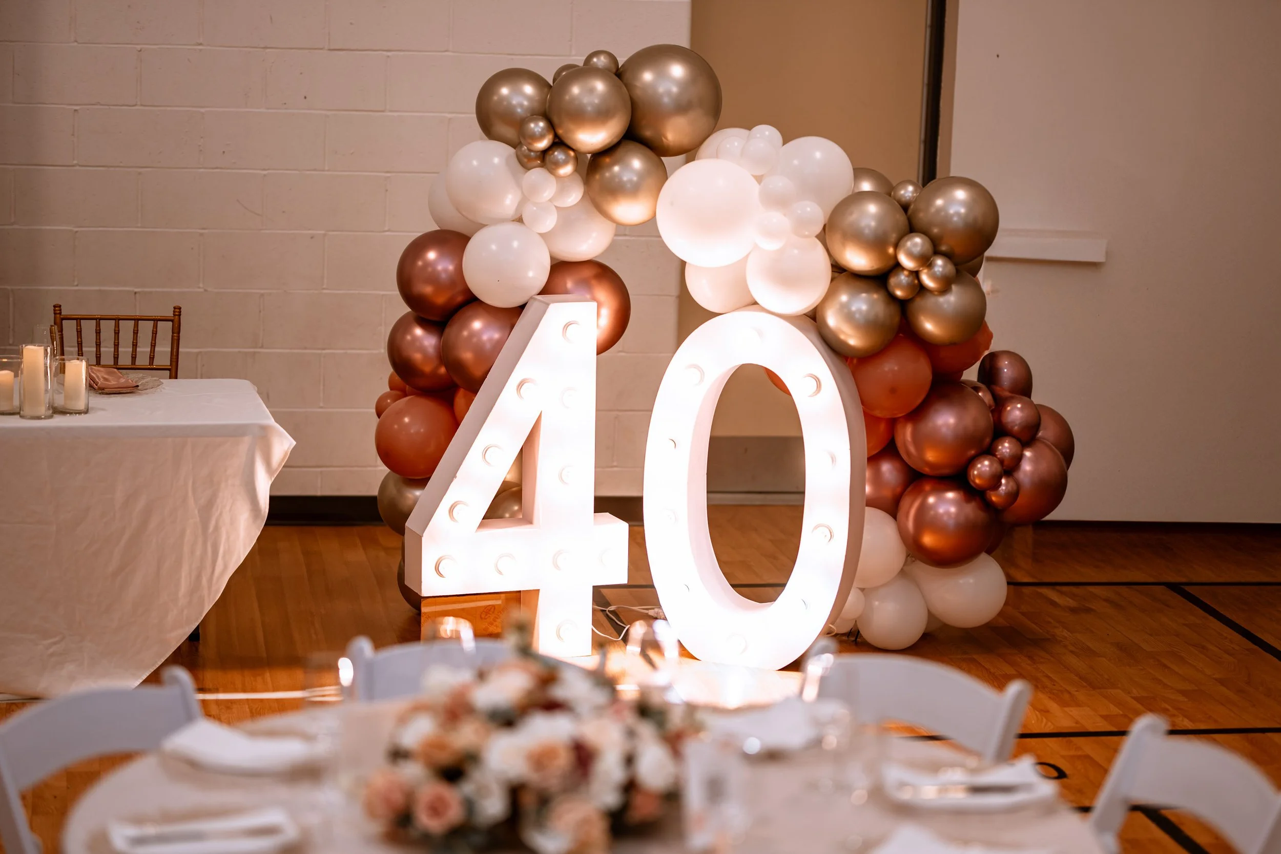 Large illuminated number 40 with balloon arch in gold, white, and bronze for celebration or birthday party.