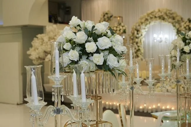 Elegant wedding table centerpiece with a large bouquet of white roses surrounded by tall glass candle holders and white candles