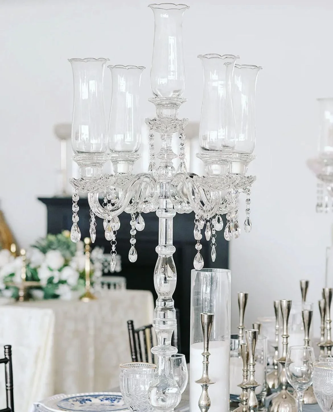Elegant crystal chandelier with multiple glass arms and hanging crystal decorations, placed on a dining table with candles and glassware in the background.
