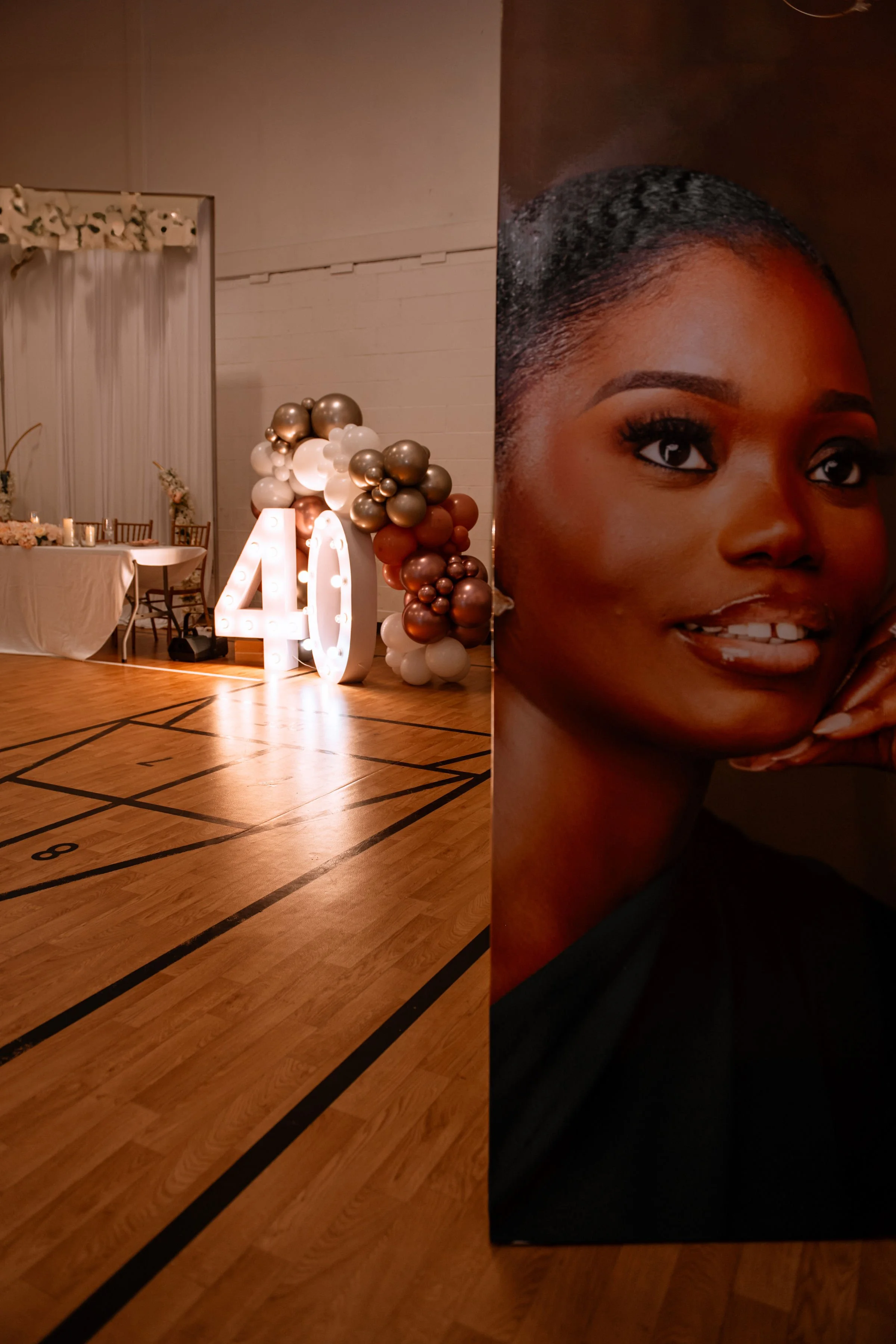 Decorated indoor event space with balloons, a large illuminated '40' sign, a table with chairs, and a wall with sheer curtains.