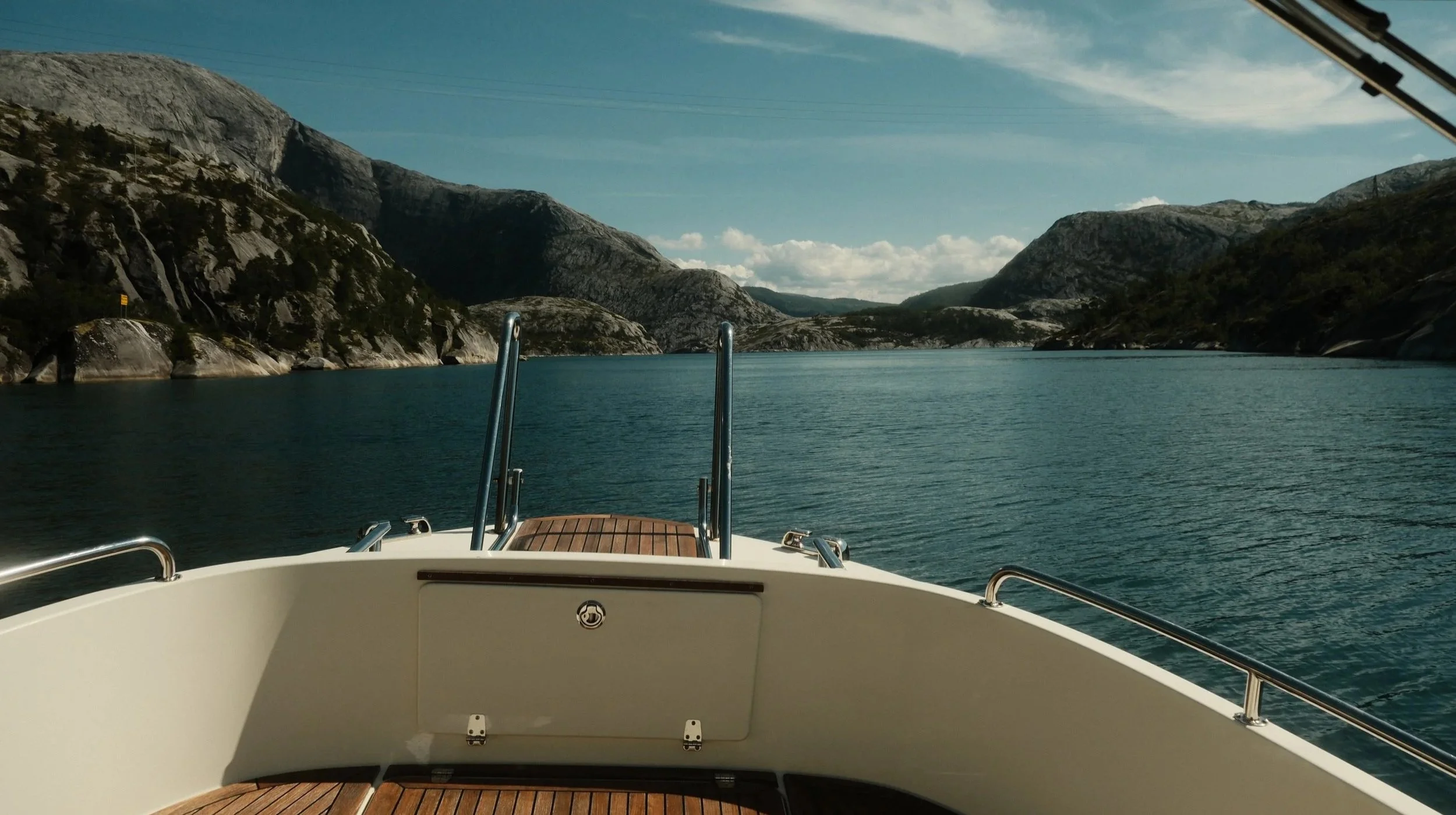 Båt på en rolig fjord omgitt av høye, fjellrike kystlinjer under en klar dag.