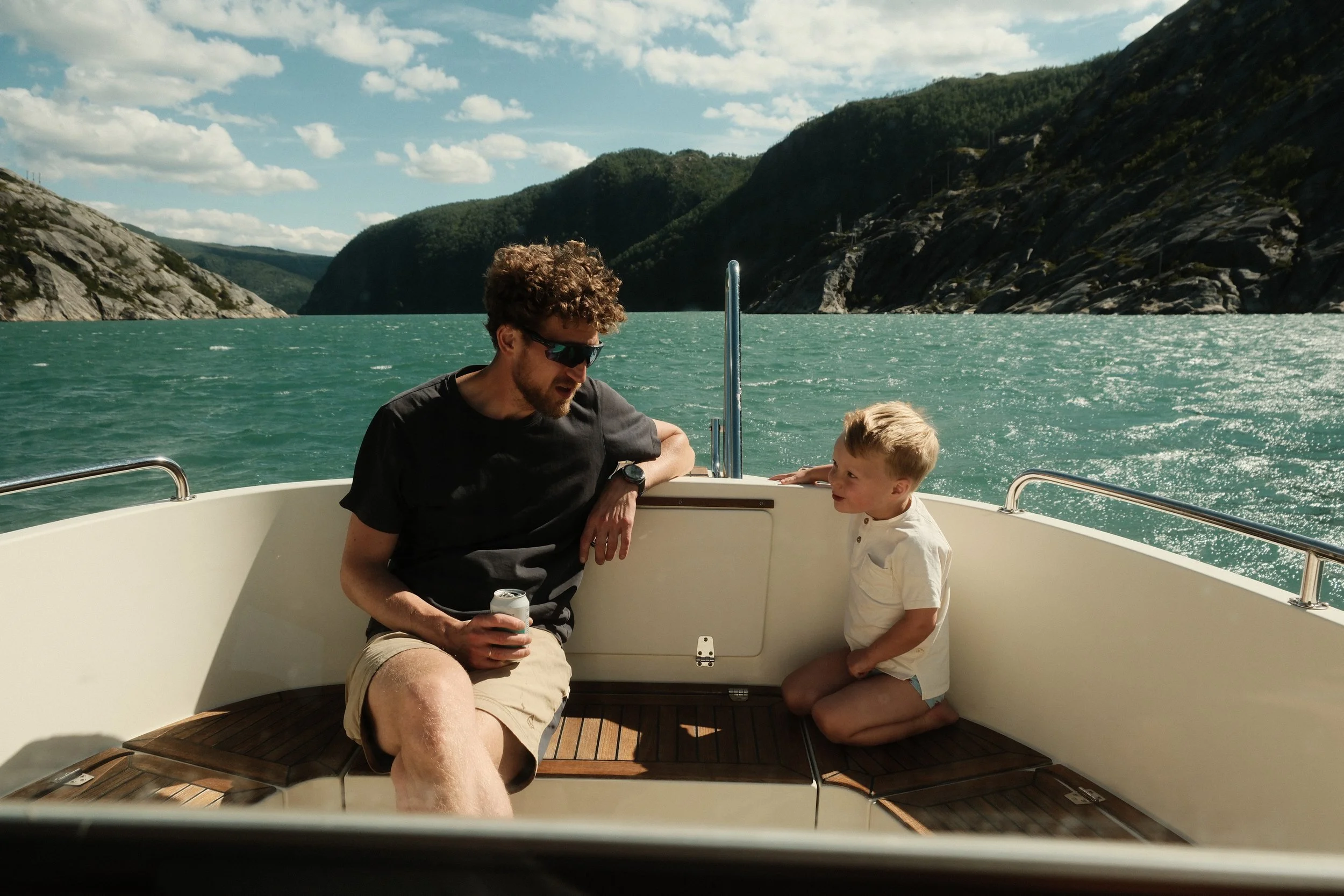 En mann og en ung gutt snakker på en båttur i en innsjø omgitt av grønne fjell.