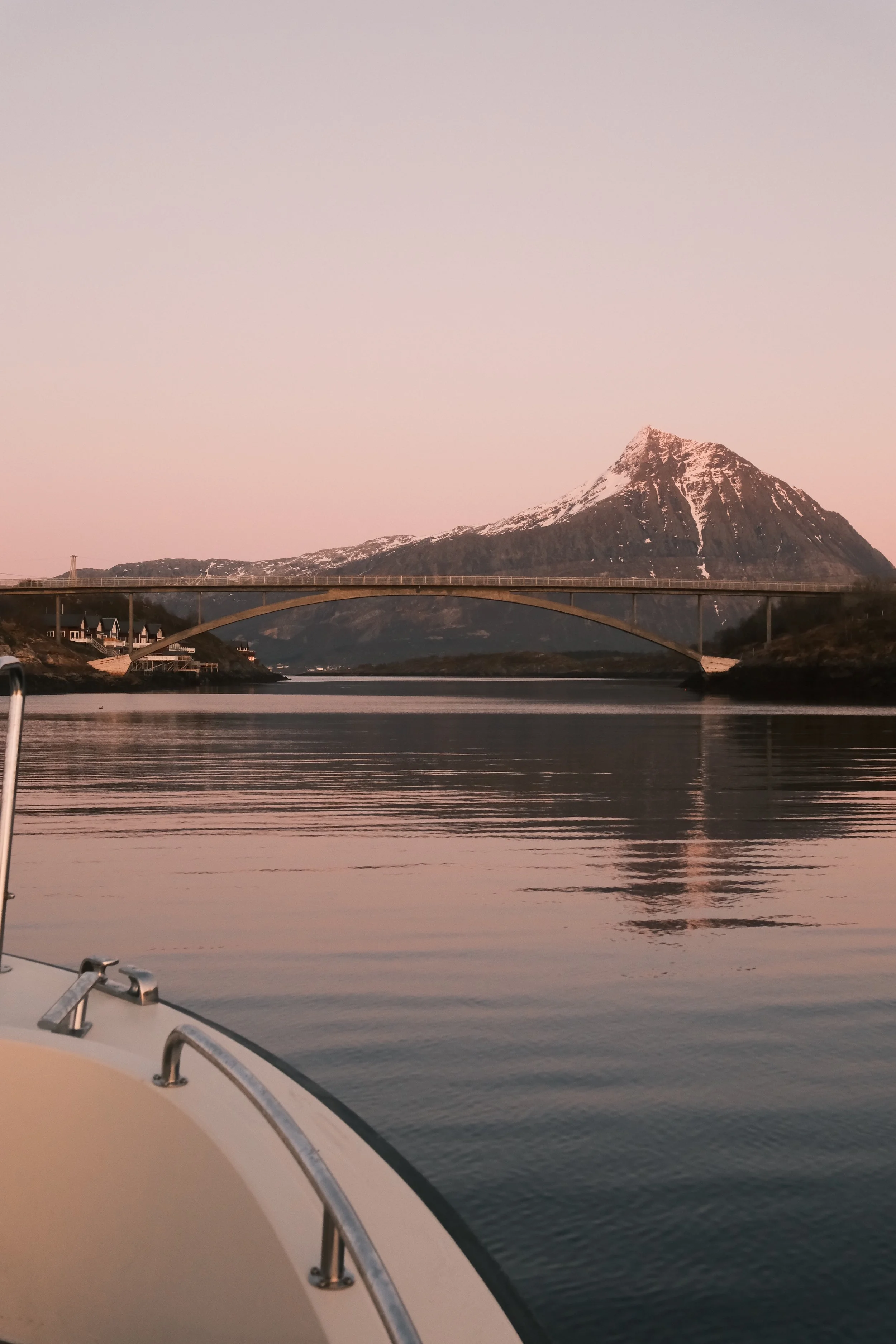Utsikt fra baugen på ATLAS mot fjellene og broen i Arnøysundet – stille hav og arktisk landskap.
