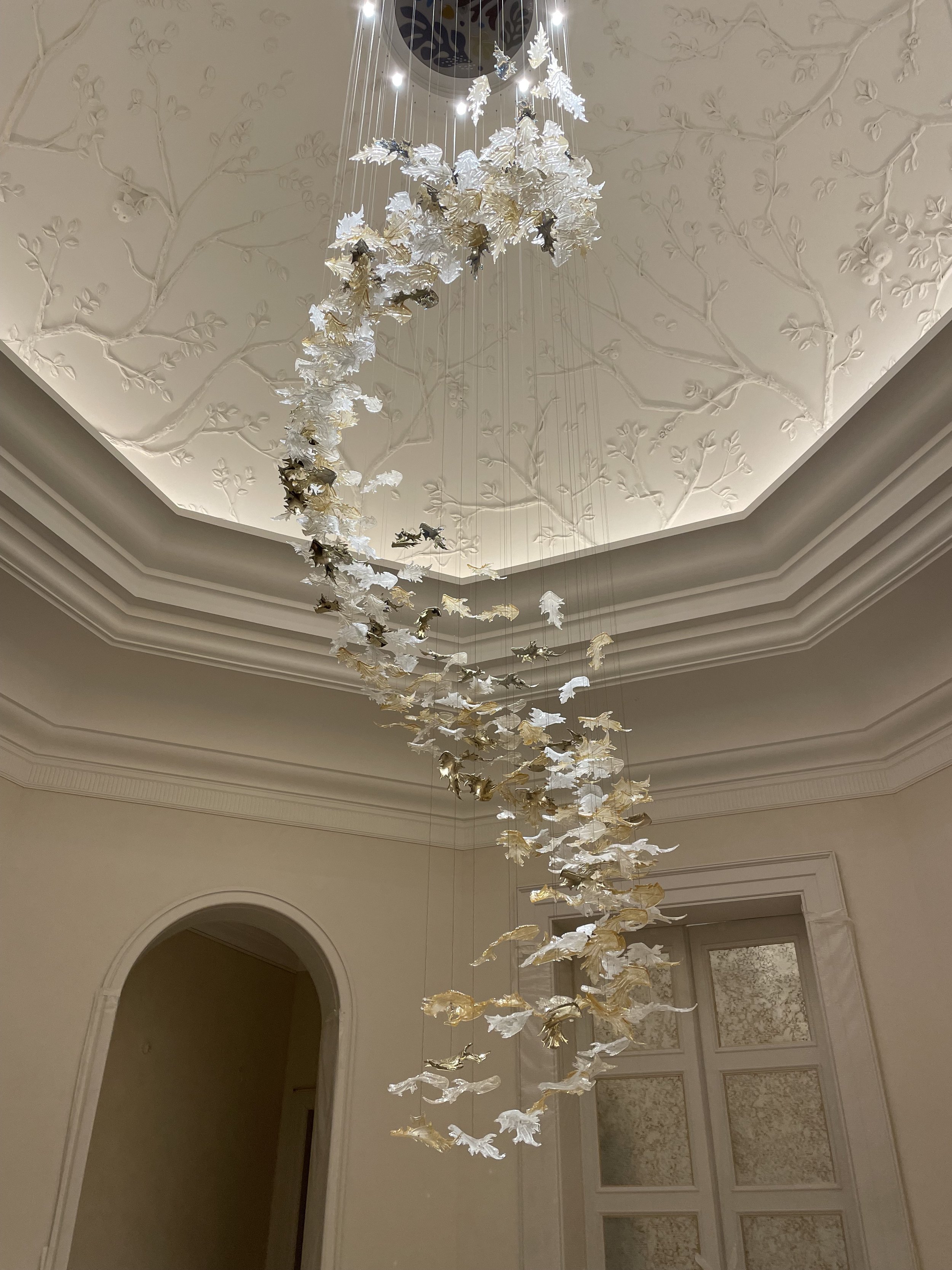 Lustre suspendu orné de motifs décoratifs blancs et dorés dans un intérieur à plafond mouluré.