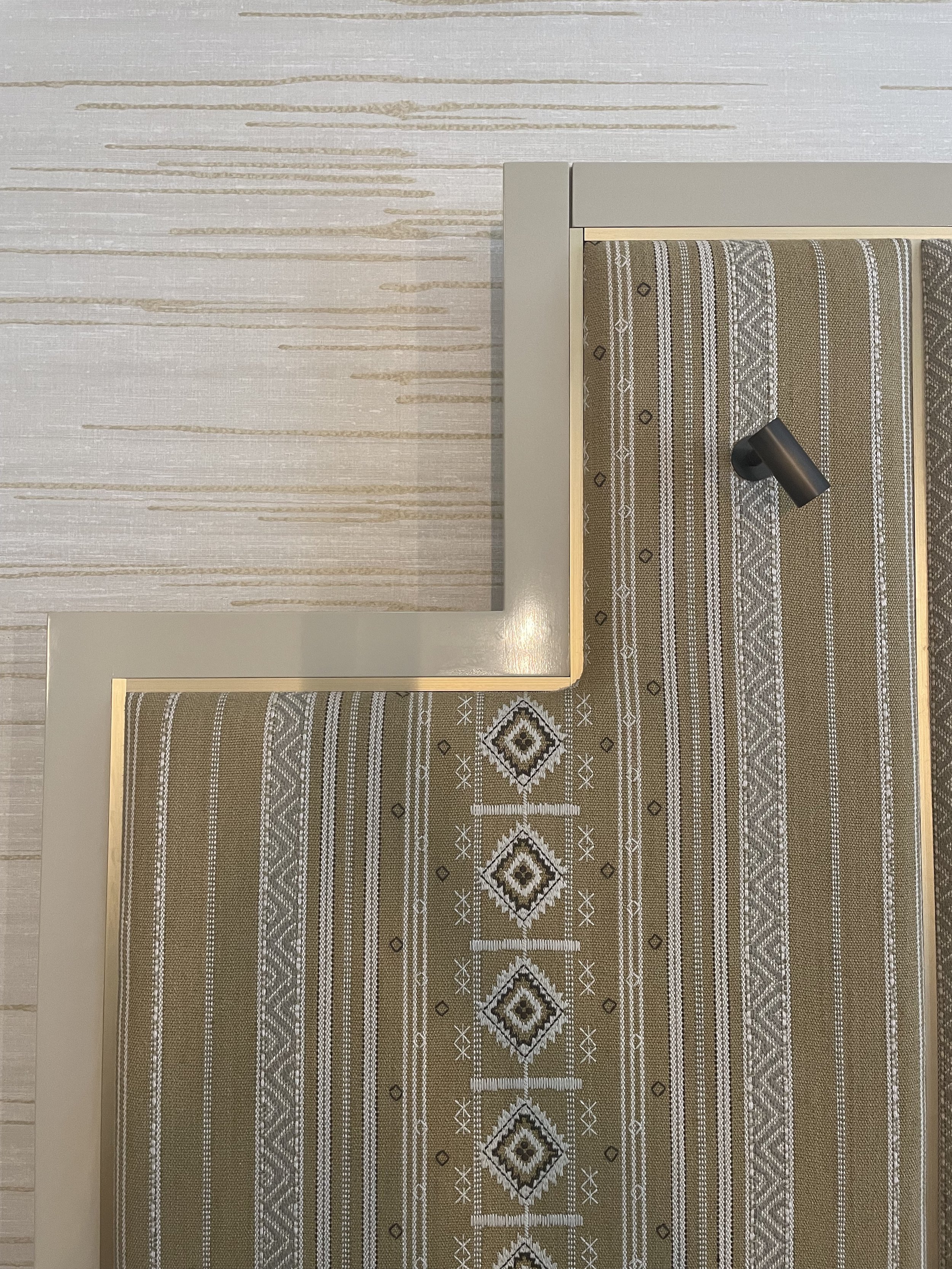 Encadrement beige avec tissu à motifs géométriques et crochet noir.