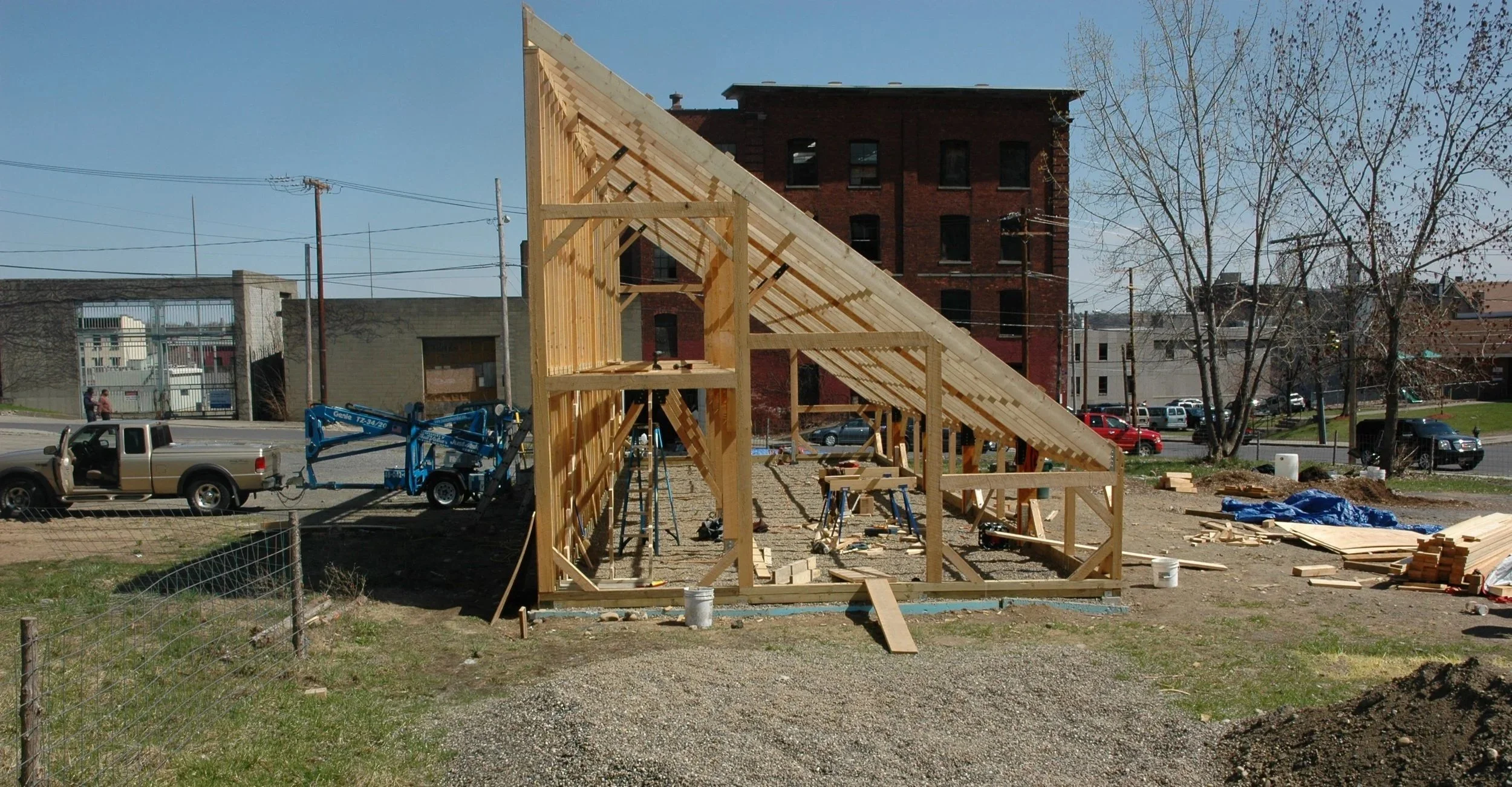 Construction site with the wooden framing of a building, construction tools, and vehicles, including a truck and a blue lift, in an urban area.
