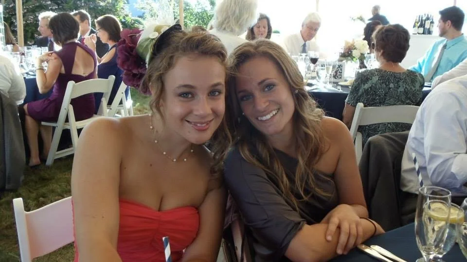 Two young women smiling at a banquet table during a formal event.