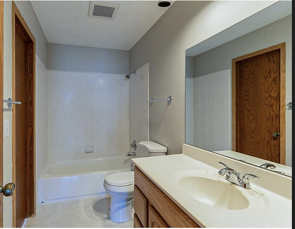 Empty bathroom with a bathtub, toilet, wooden door, and a large mirror above the sink.