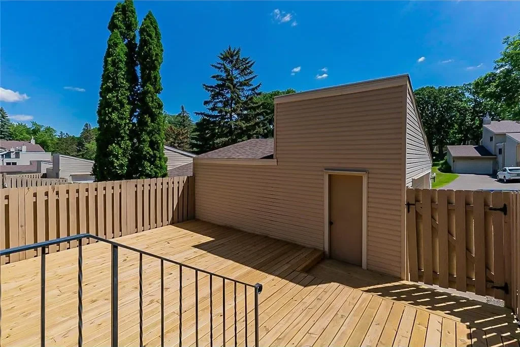 Wooden deck with a small shed attached to a fence, in a residential backyard with trees and neighboring houses.