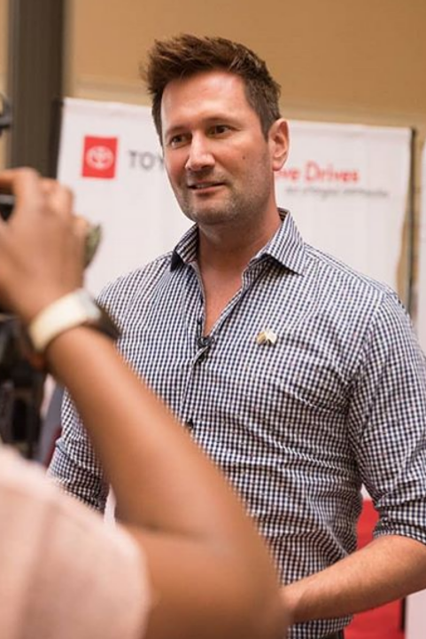 Adventure Scholars co-founder, Justin Leach wearing a checkered shirt being interviewed by media at an event.