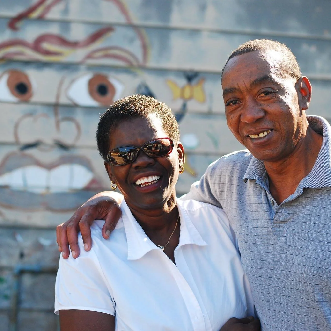 Adventure Scholars advisors, Mary and Sylvester Hoover smiling with arms around each other, in front of a mural with a face and a butterfly.