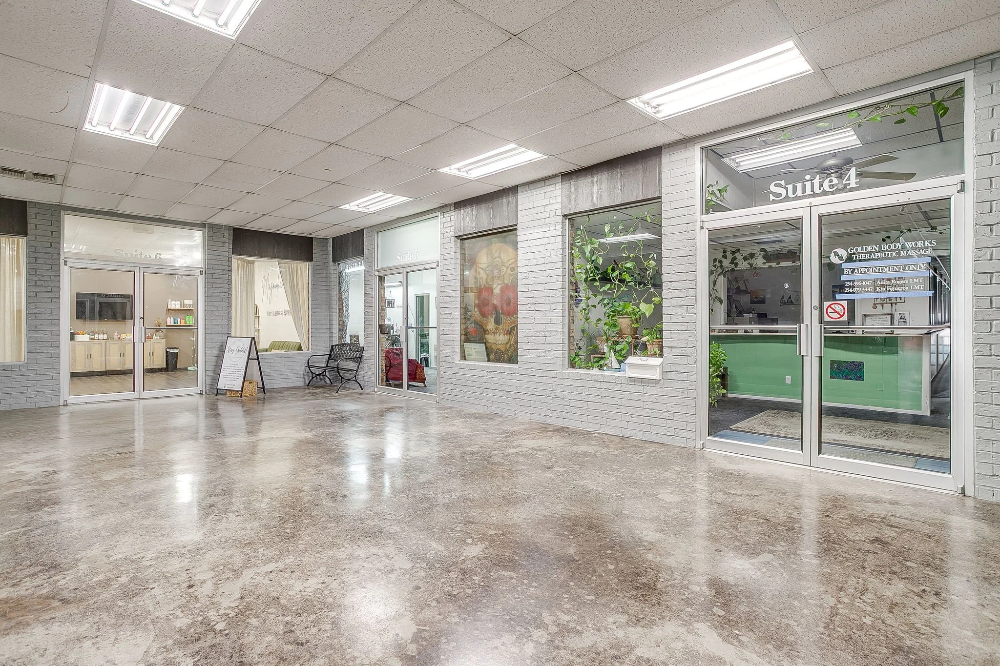 Interior of a building with small commercial suites, white painted brick walls, large windows, fluorescent lighting, and a polished concrete floor.