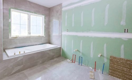 Partially renovated bathroom with bathtub, tile flooring, green drywall, and plumbing exposed.