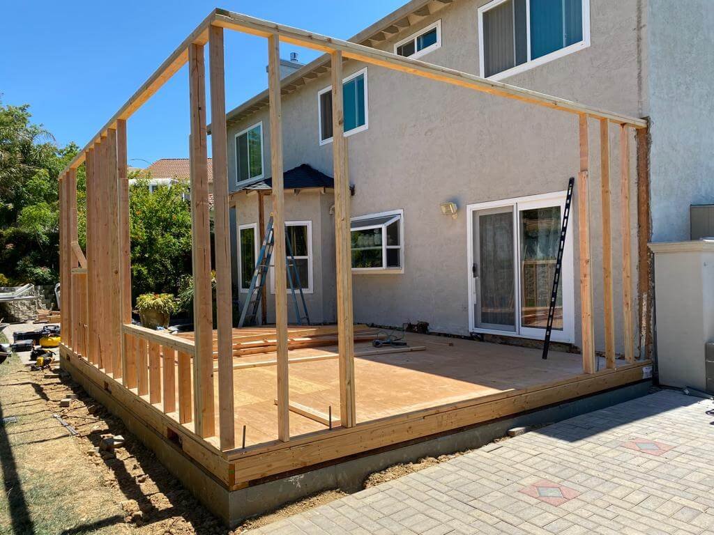 Home construction project, wooden frame structure, attached to house, sliding glass door, patio area.