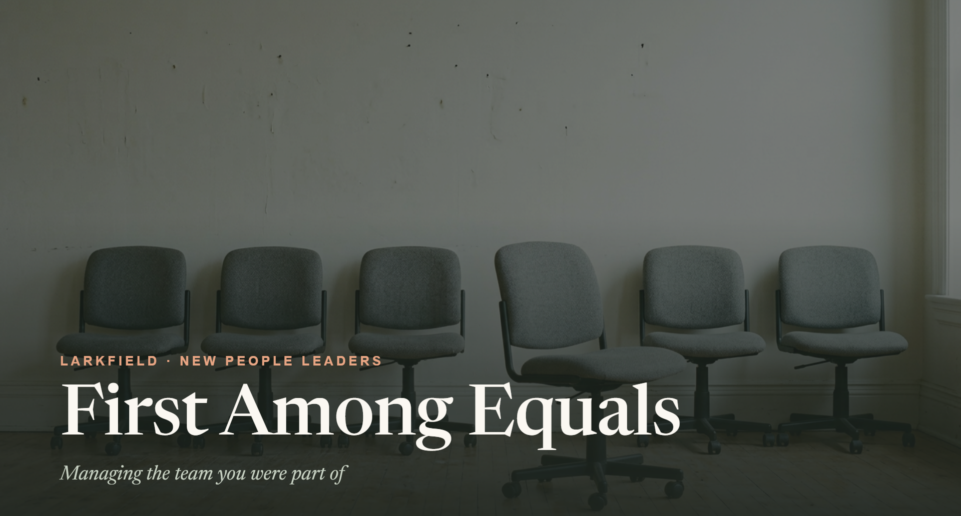 Empty chairs in a waiting room with a large window on the right and a plain wall with some marks in the background.