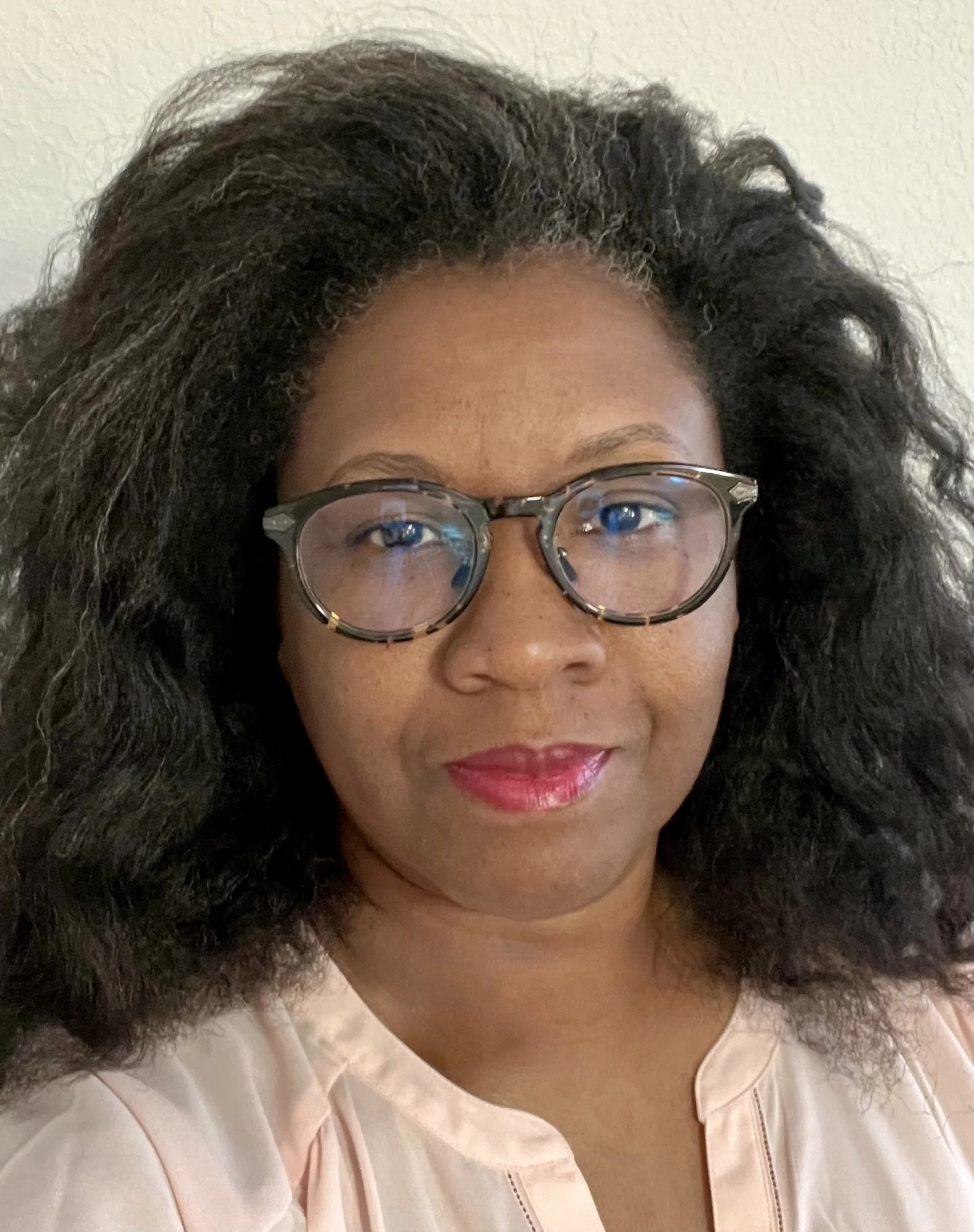 Person with glasses and curly hair wearing a light-colored top.