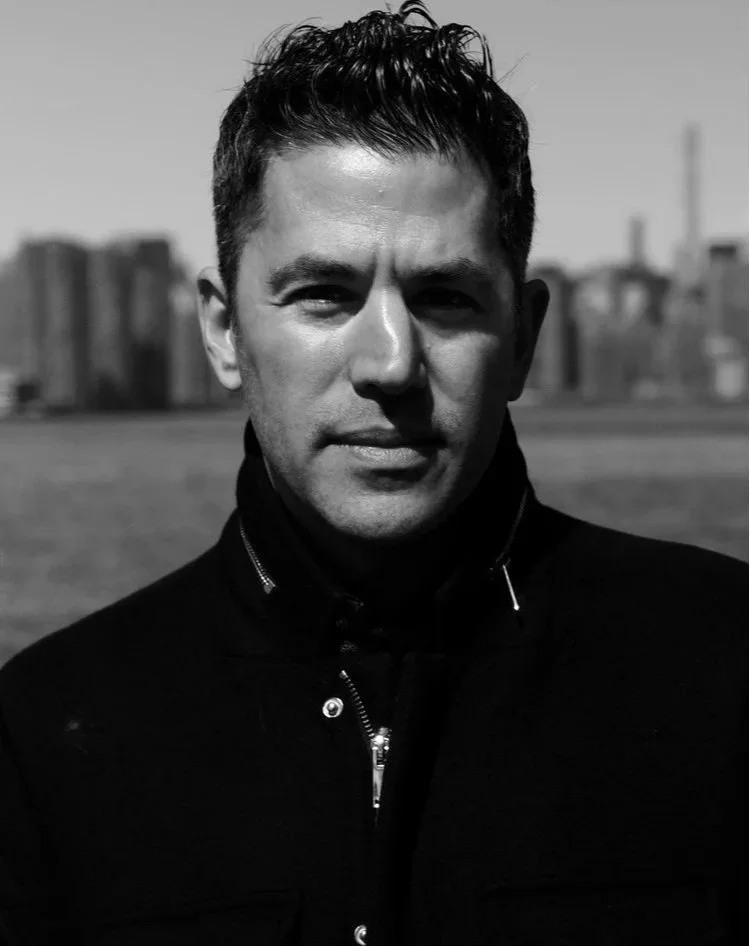A black and white portrait of a man outdoors, with the city skyline in the background.