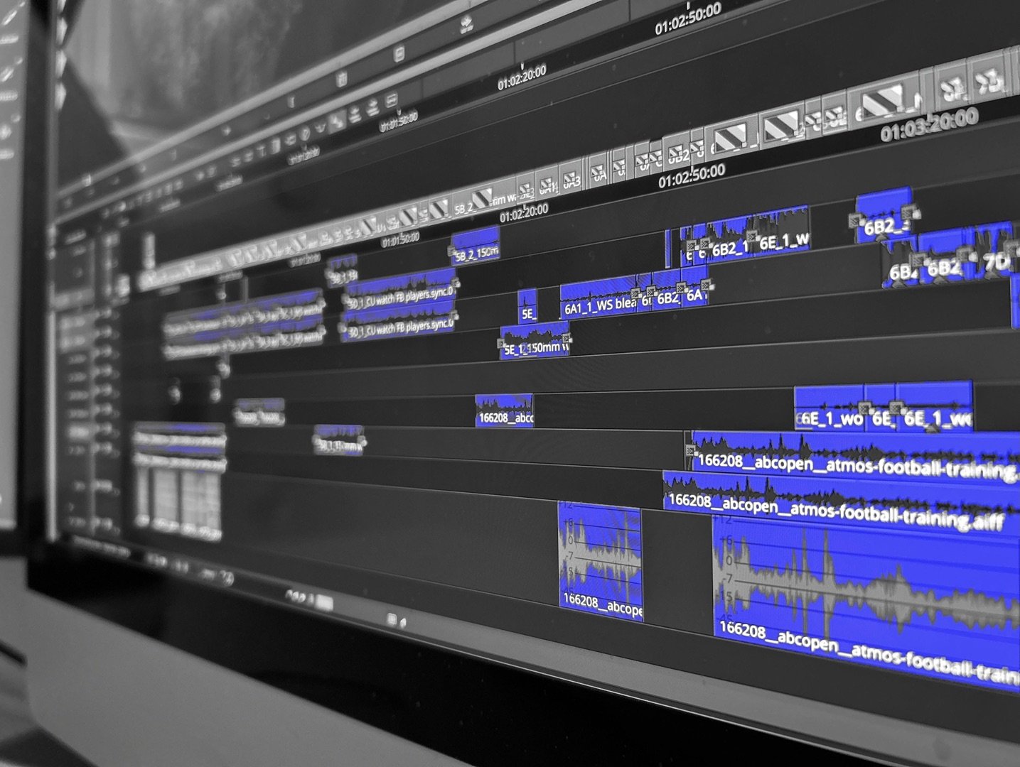 A computer screen displaying a multi-layered video editing timeline with various clips, audio tracks, and editing tools, primarily in black and blue.