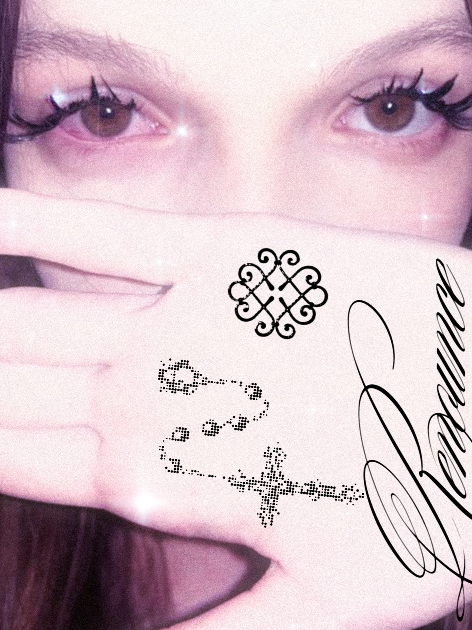 Close-up of a woman's face with brown eyes and long eyelashes. She holds her hand up in front of her face with fingers extended, showing long, nude-colored nails and decorative tattoos on her hand. The image has a pinkish filter with sparkles, and th