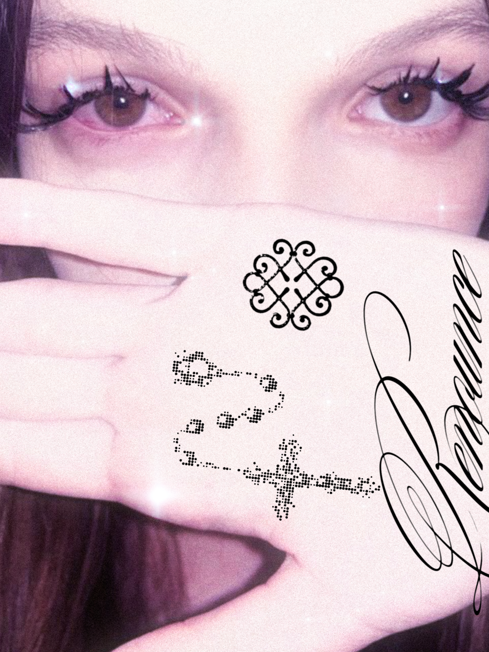 Close-up of a woman's face with brown eyes and long eyelashes. She holds her hand up in front of her face with fingers extended, showing long, nude-colored nails and decorative tattoos on her hand. The image has a pinkish filter with sparkles, and th