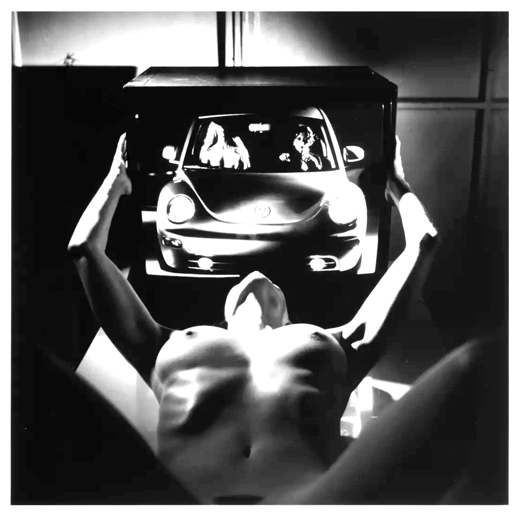 A woman lying down with her arms raised holding a picture frame of a car and two people inside it.