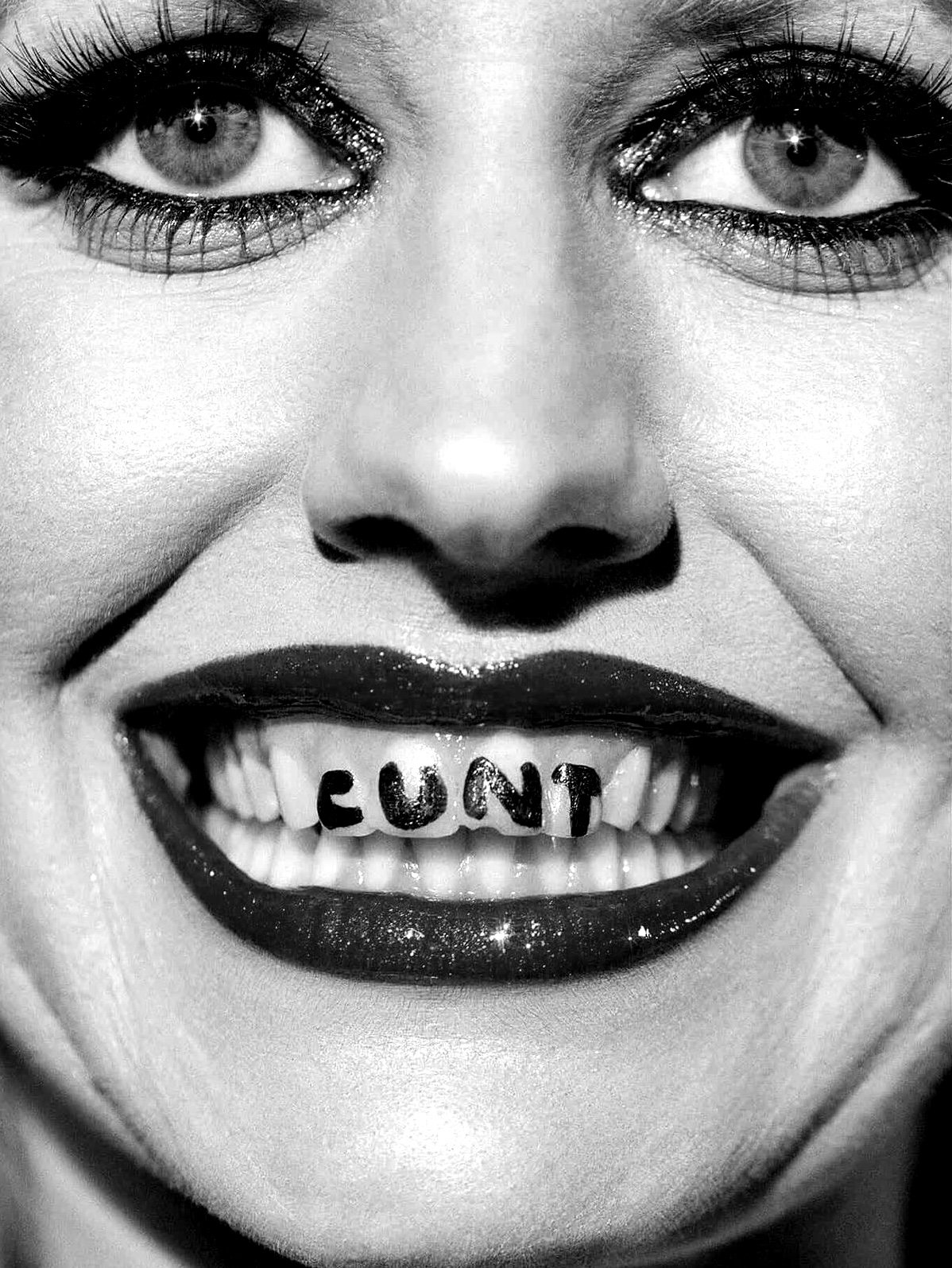 Close-up of a woman's face in black and white, showing eyes with makeup, a nose, and a mouth with lipstick. The teeth spell out the word 'CUNT'.