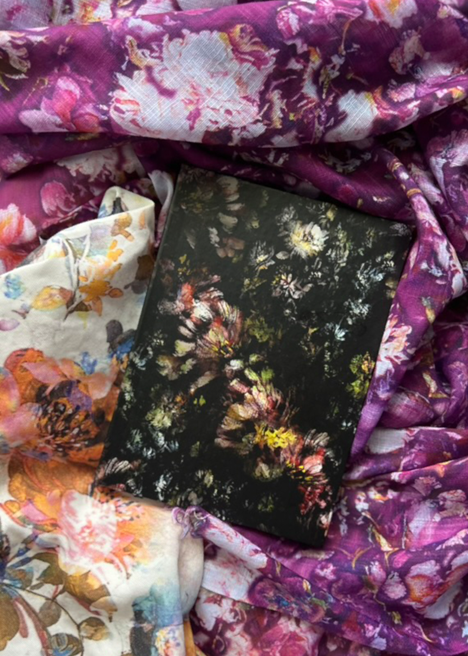 A floral notebook resting on colorful floral fabric.