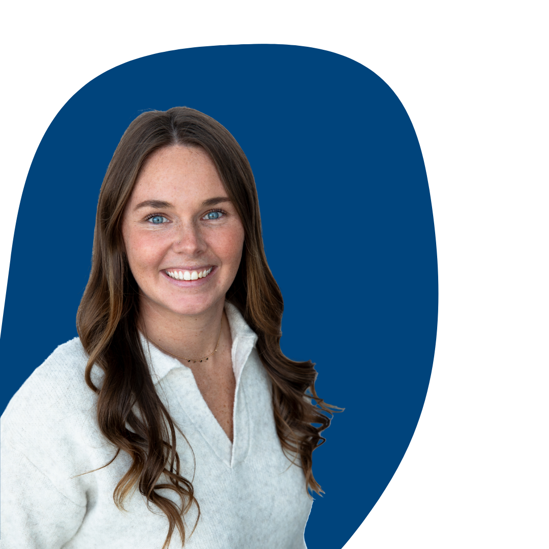 Smiling young woman with long brown hair and blue eyes, wearing a white sweater, against a simple background.
