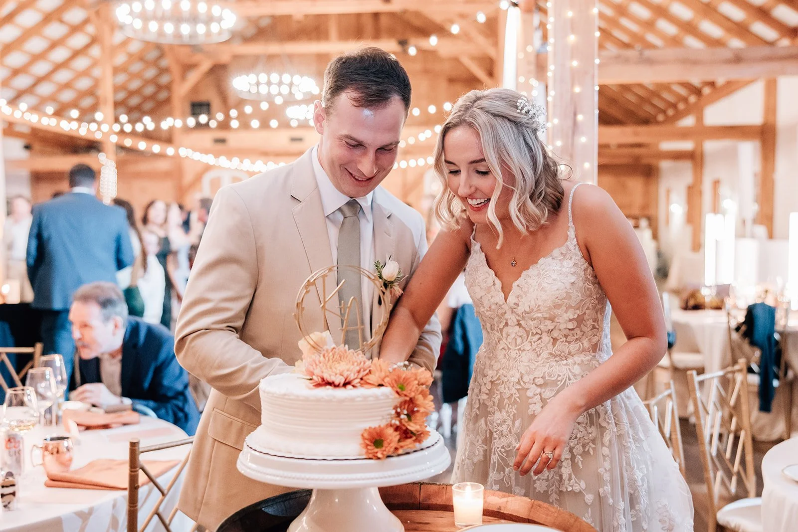 A bride and groom cut their wedding cake together in a decorated venue with string lights and wooden architecture.