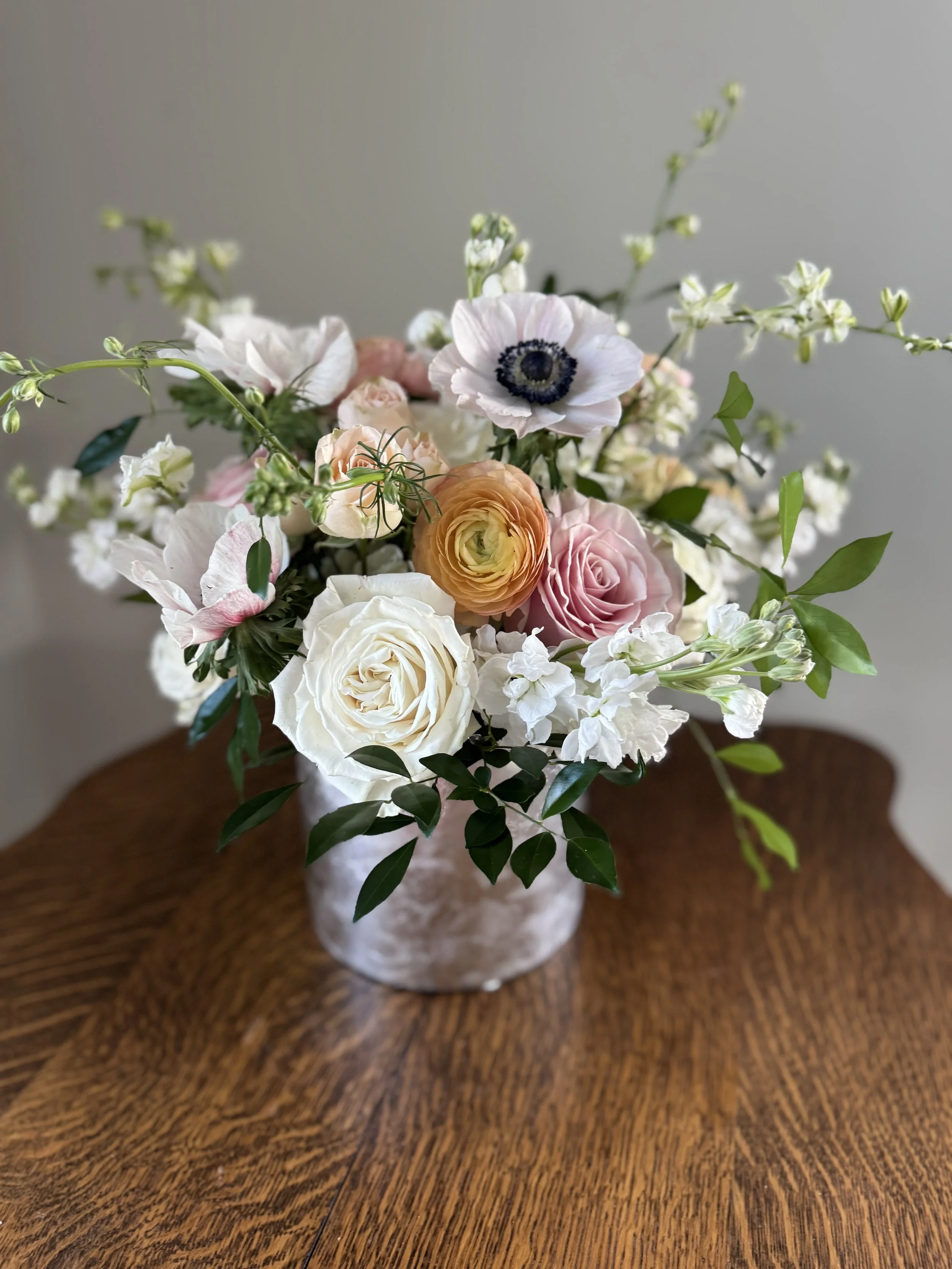 Flower arrangement with roses, anemones, and ranunculus in a vase on a wooden table.
