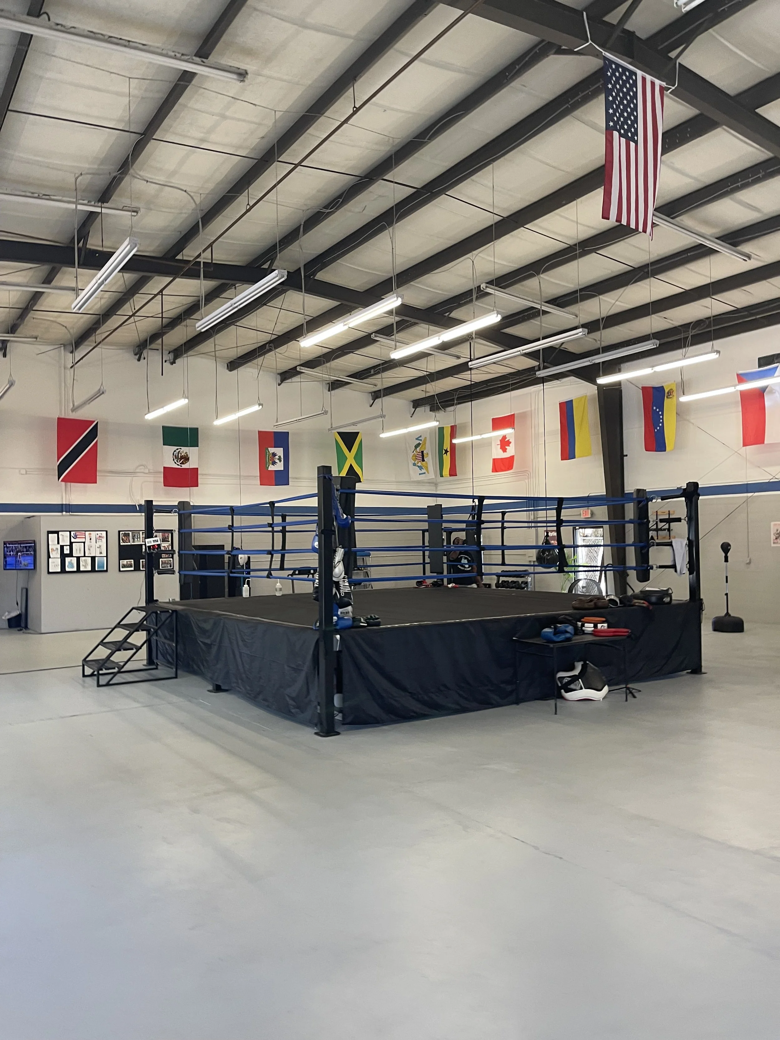 An empty boxing ring inside a gym with American flags hanging from the ceiling.