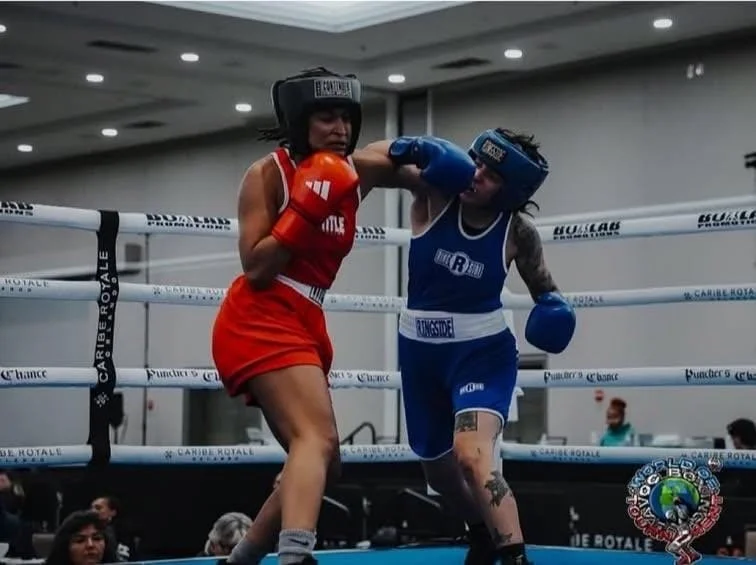 Two women boxers in a ring, one in red and the other in blue, engaged in a match during a boxing event.